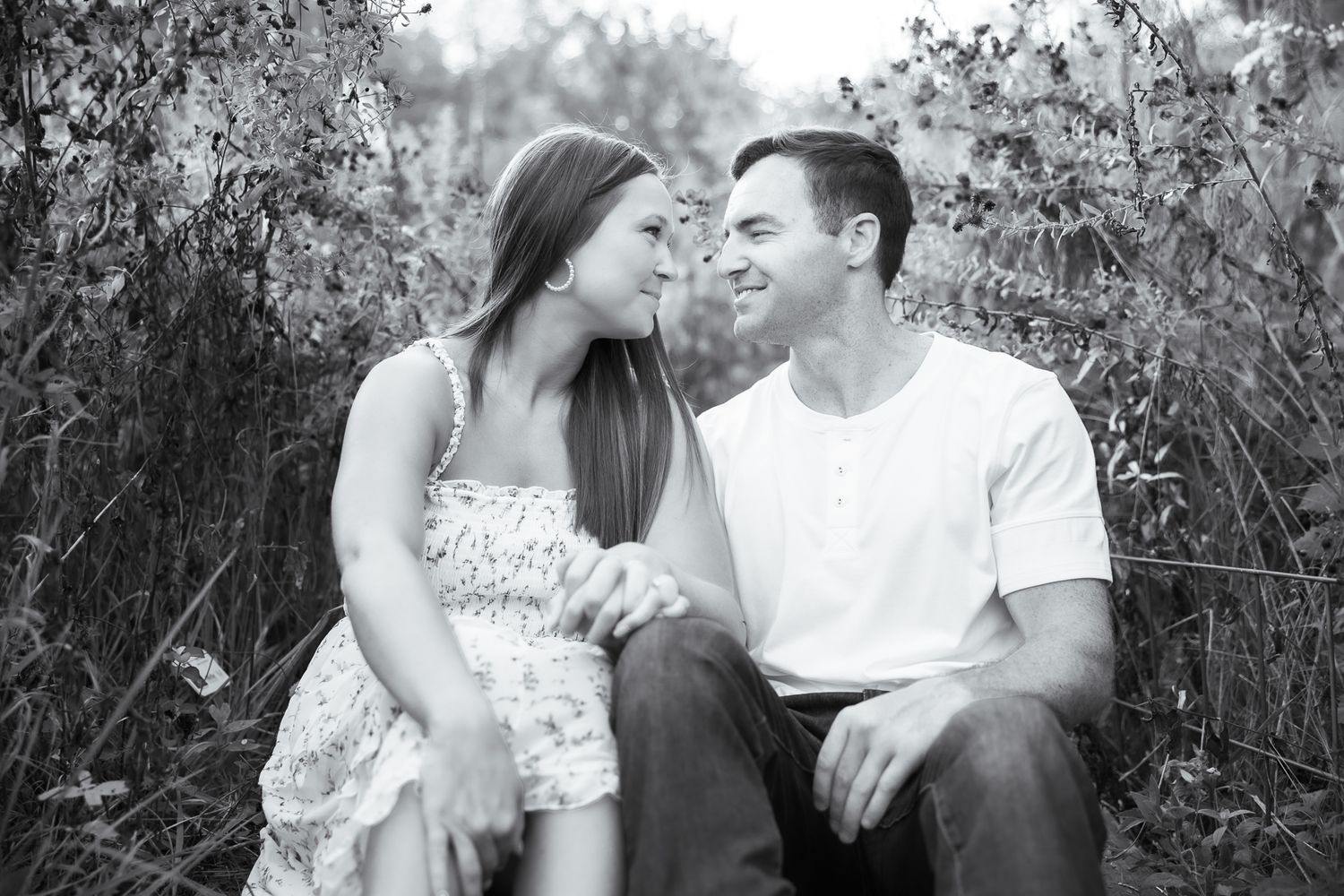 A couple shares intimate moments while sitting together outdoors surrounded by foliage.