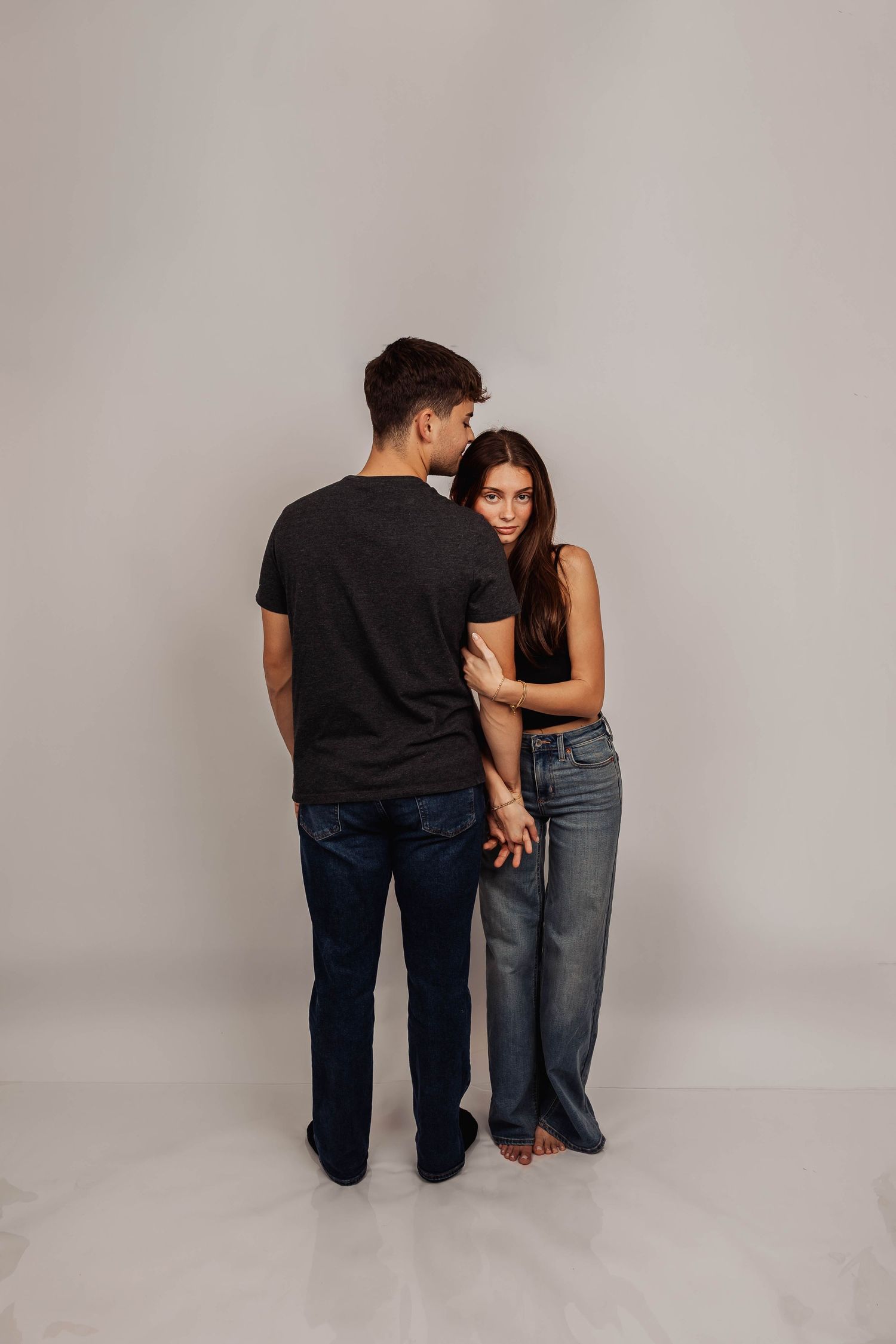 Couple in casual clothing stands close together during studio photoshoot.