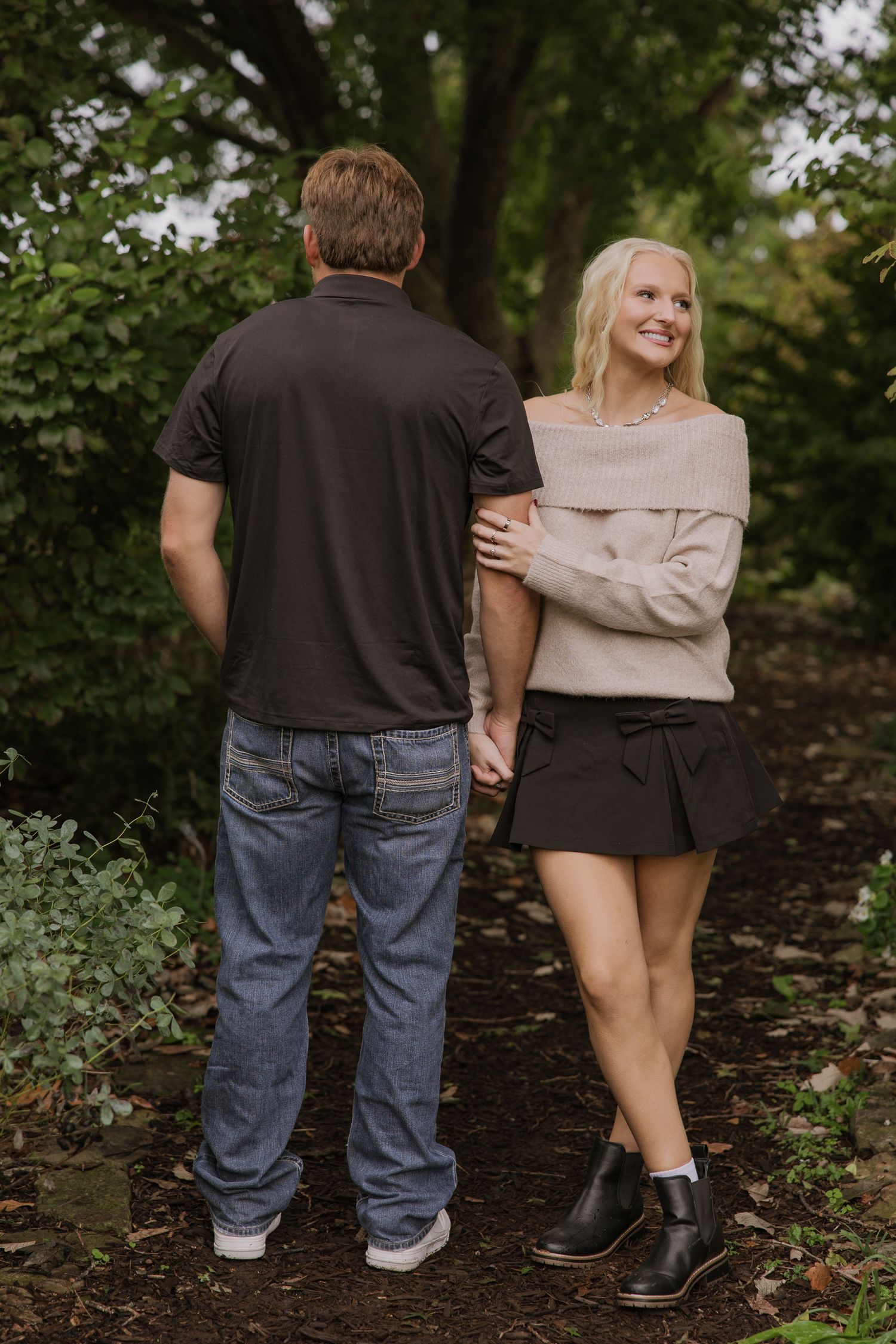 Casual outdoor portrait of a couple holding hands on a wooded path.