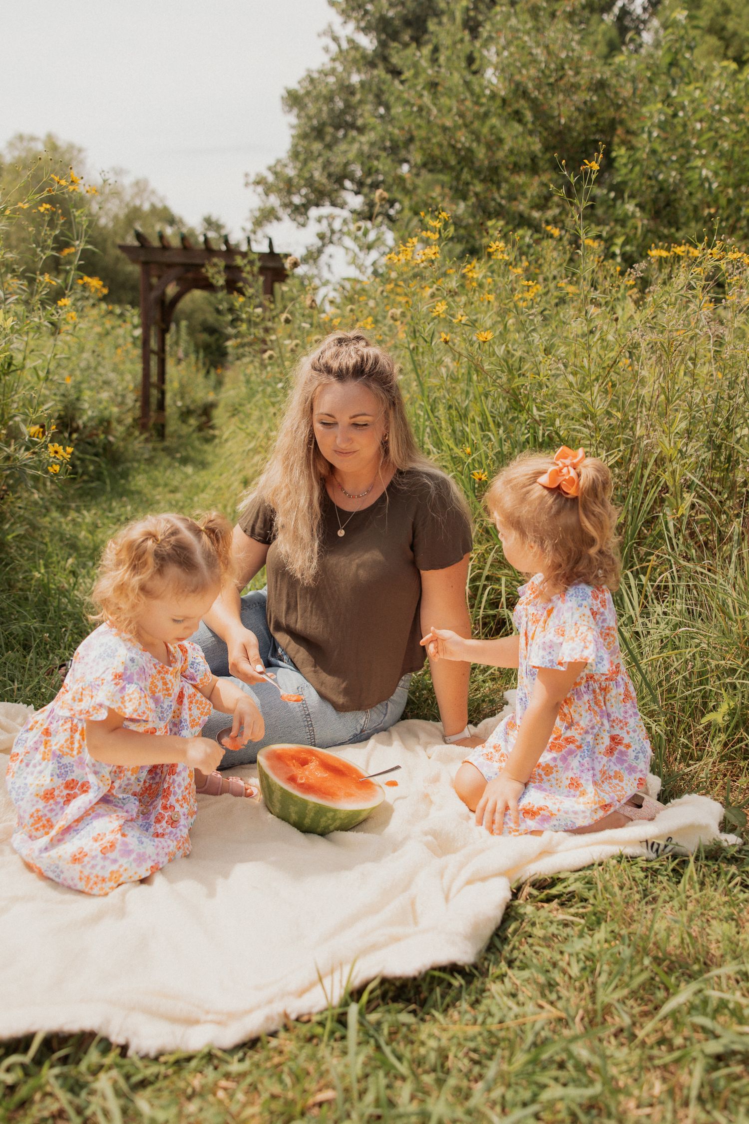A summer picnic scene with watermelon and a blanket laid out in a garden.