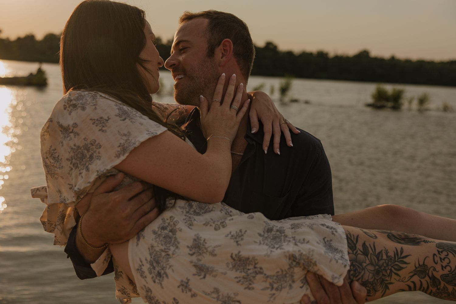Intimate moment captured during sunset beach photoshoot with water backdrop.