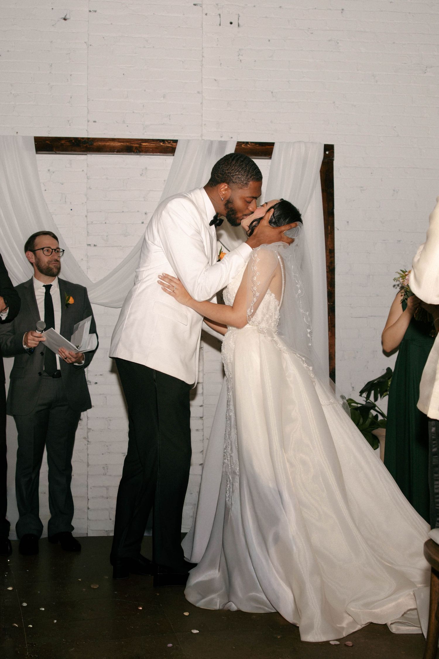 Wedding party members dance and celebrate in a white-walled venue.