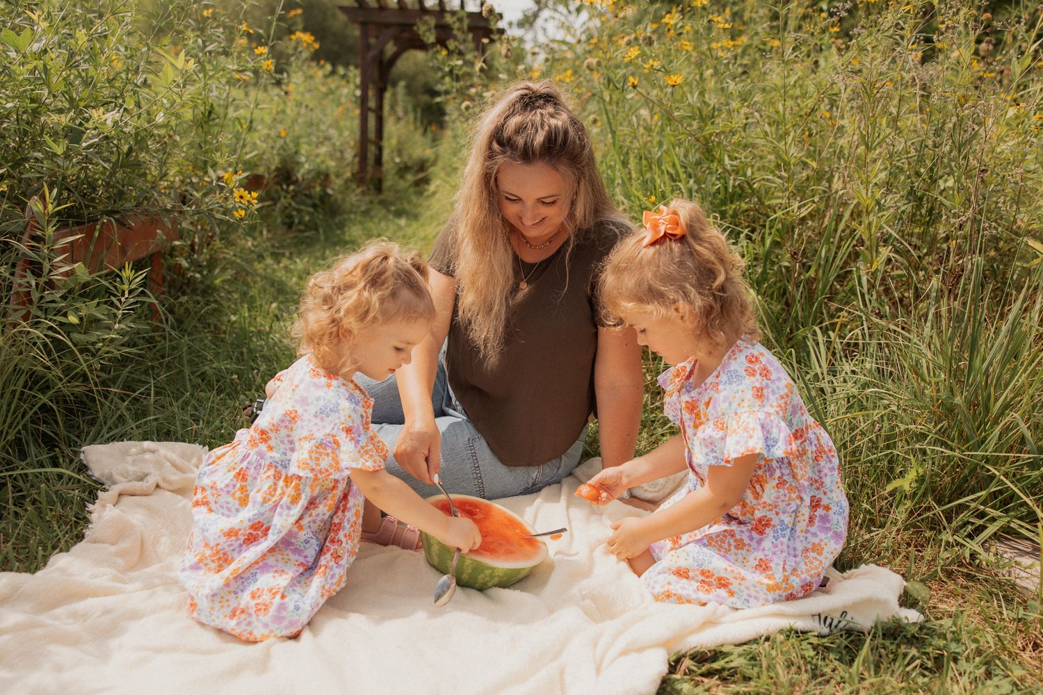 A summer picnic scene with watermelon on a blanket surrounded by yellow wildflowers.