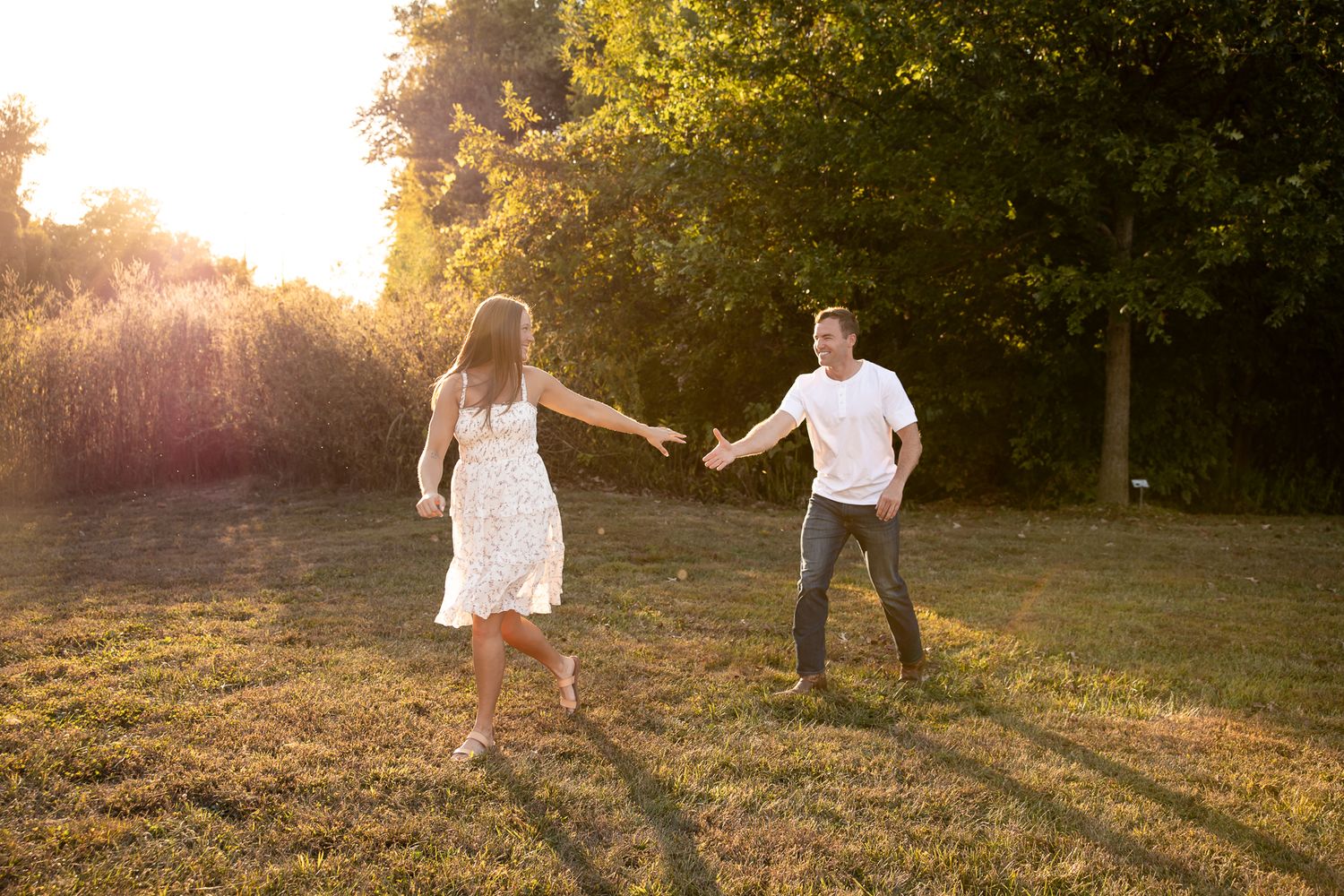 Couple playfully runs and dances in golden field at sunset.