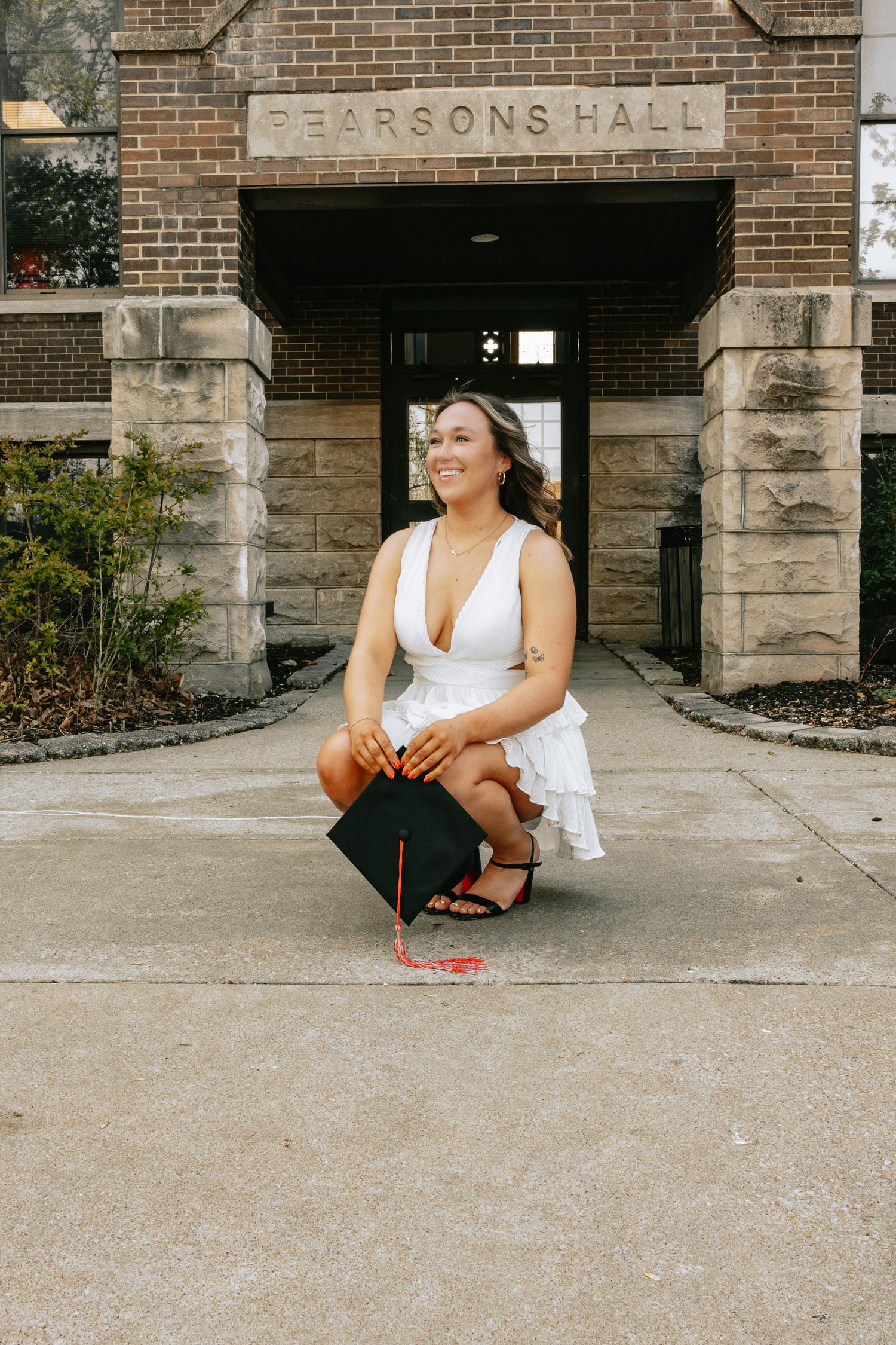 Graduate posing on steps in front of Pearsons Hall brick building.