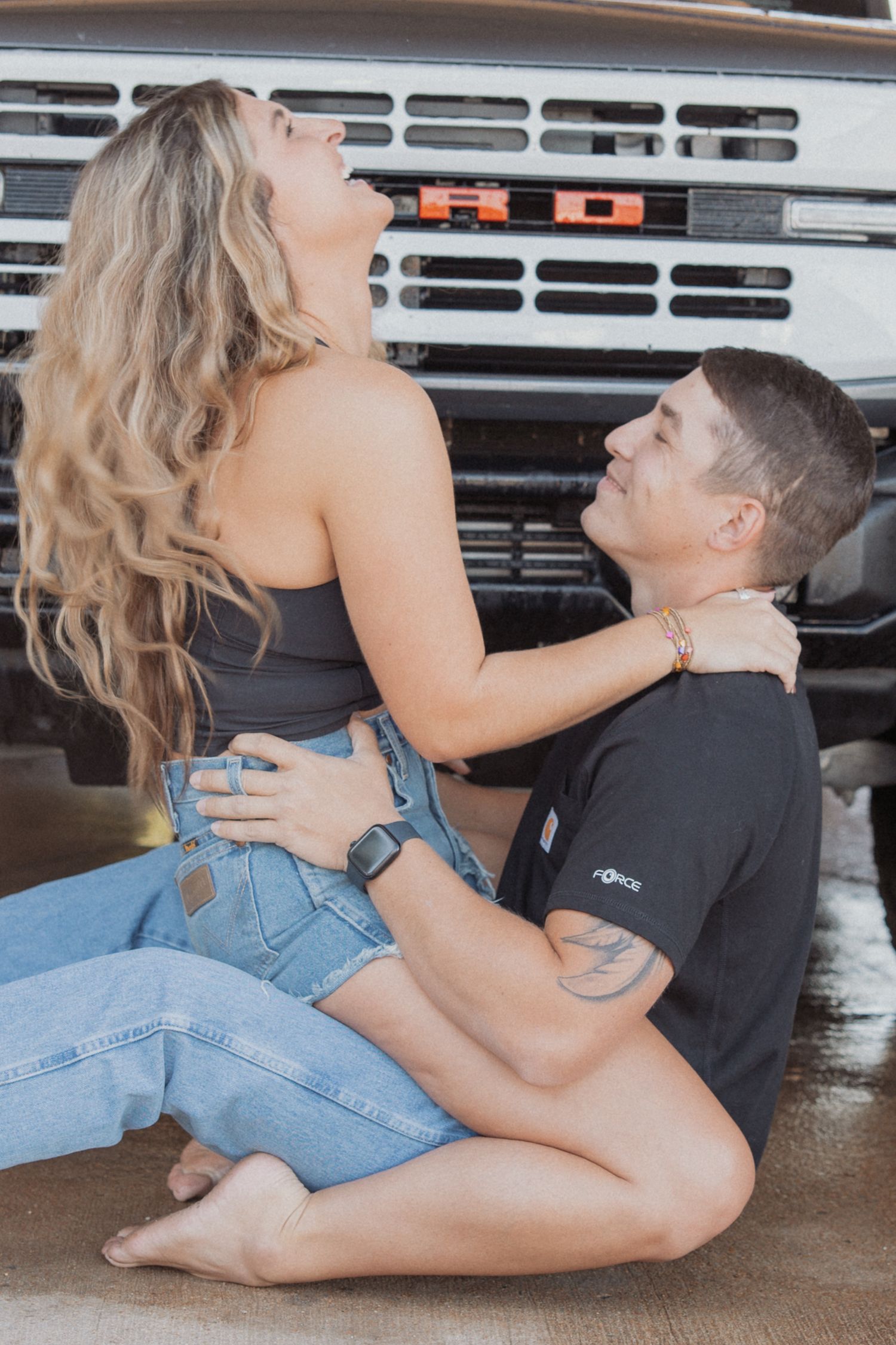 Couple in casual wear posing on garage floor near vintage truck.