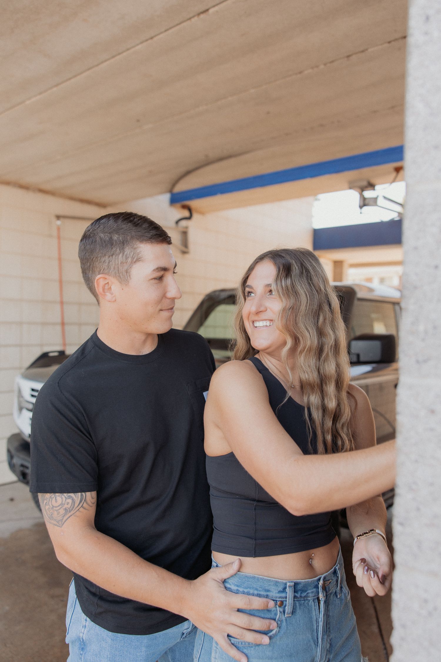 A couple in black and denim sharing an intimate moment against a concrete wall.