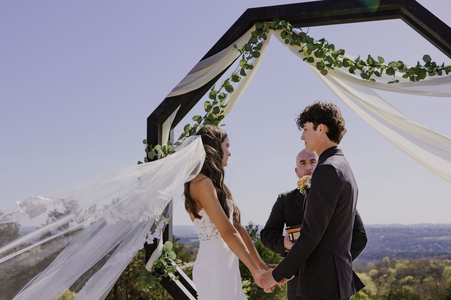 A couple exchanges vows under a decorated wedding arch with mountain views.