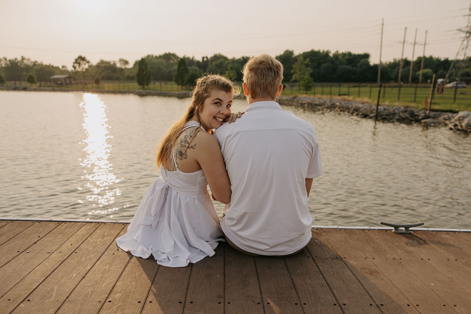 Couple sits together on wooden dock overlooking peaceful lake at sunset.