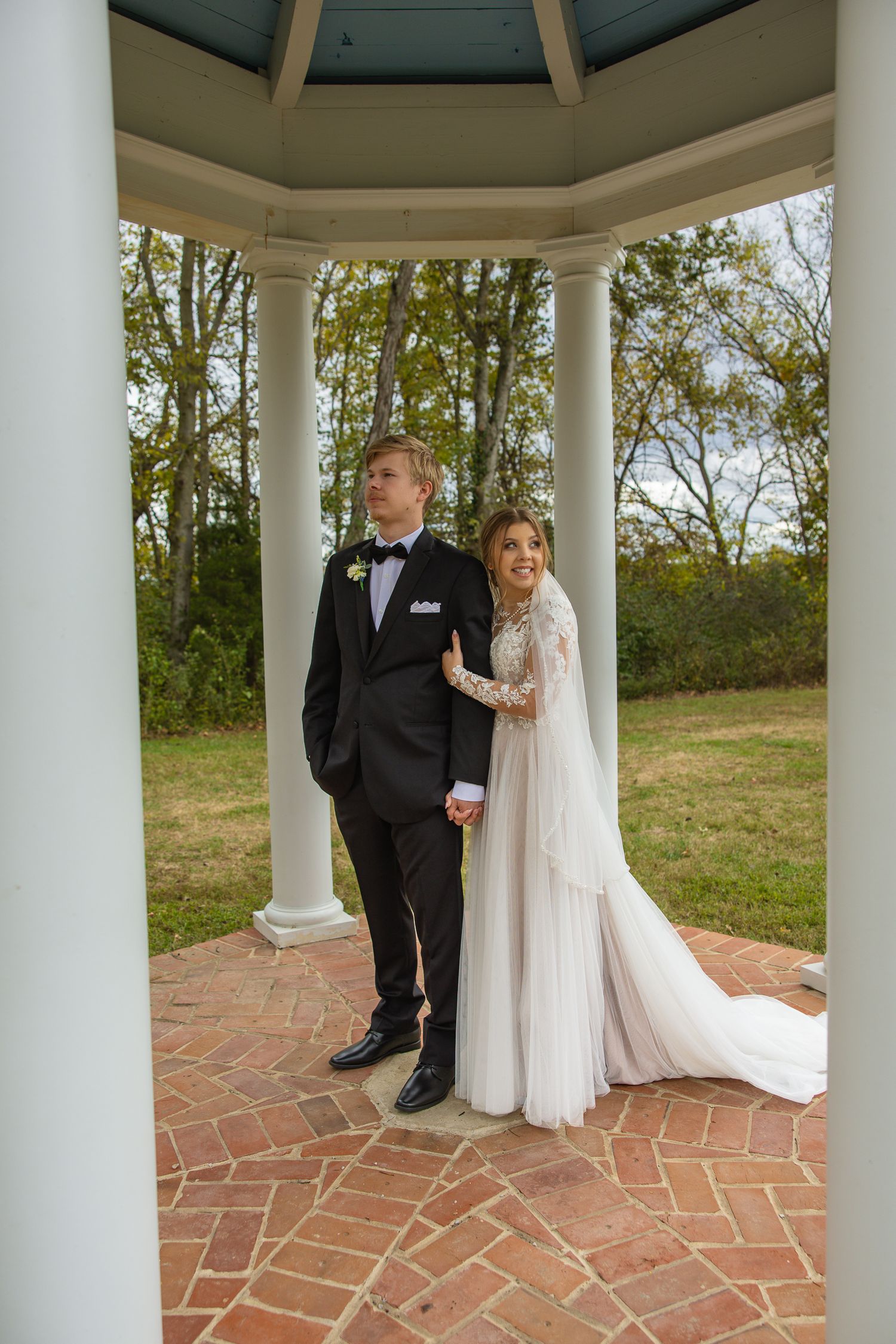 Elegant wedding portrait in a white gazebo with classic columns and brick flooring.