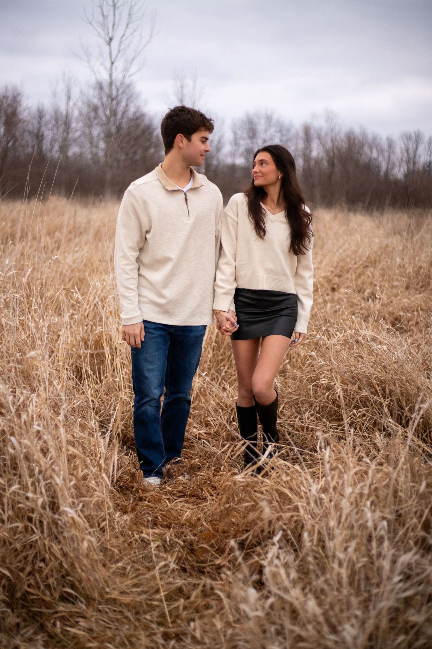 A couple walking through tall dried grass in a field wearing casual outfits during autumn.