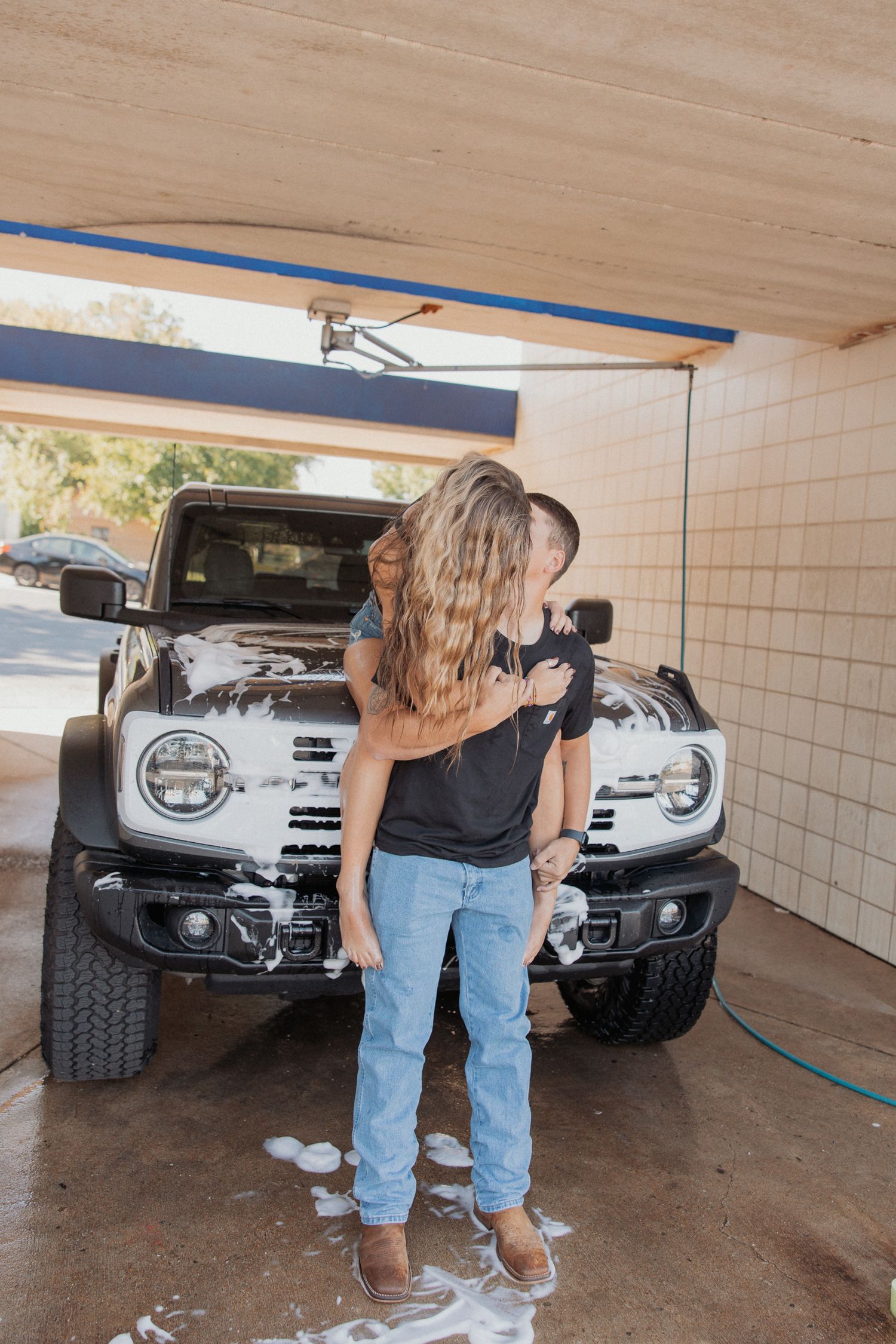 A couple stands close together in front of a silver truck in a covered parking area.