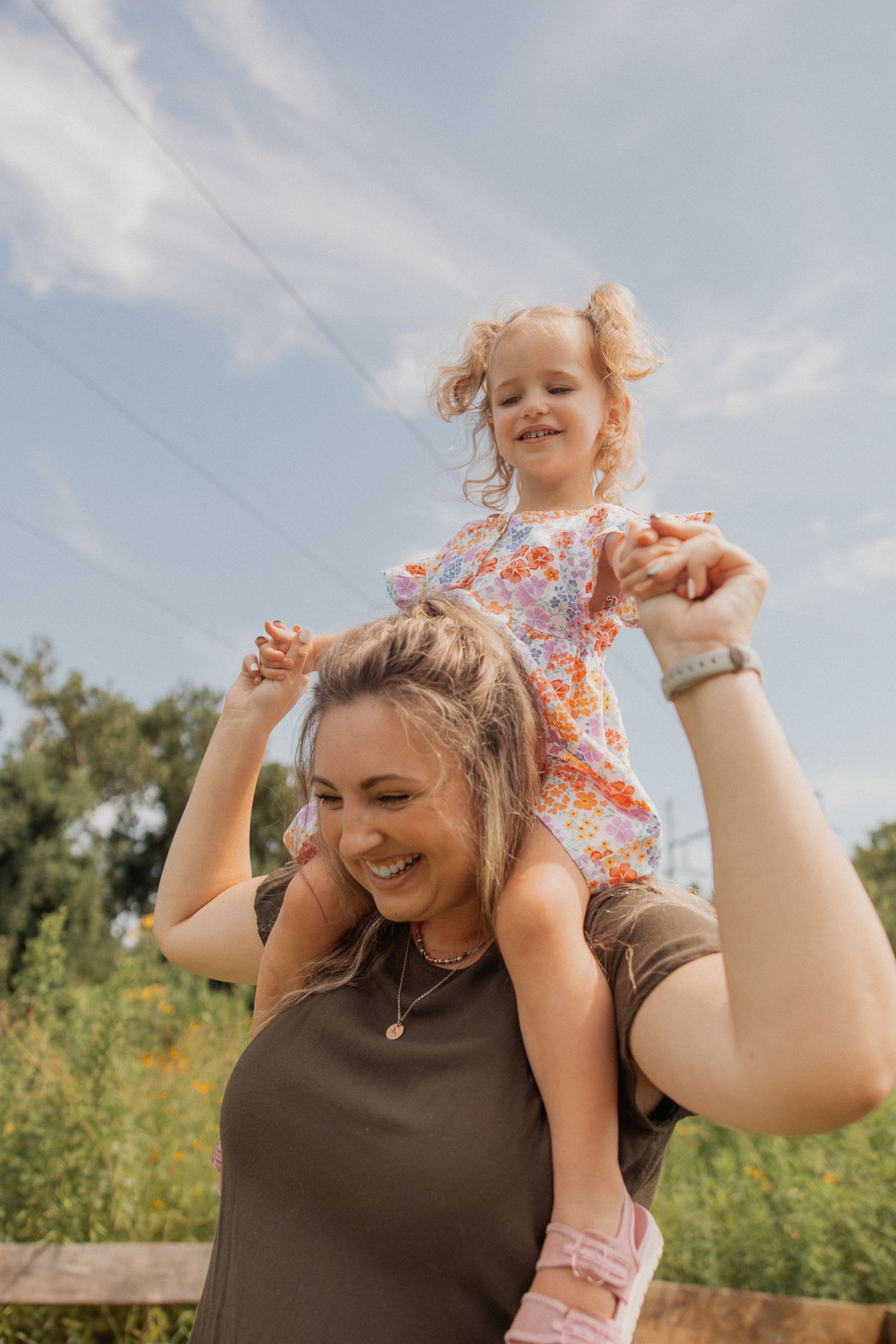Playful shoulder ride moment captured against a bright blue sky in a summer field.