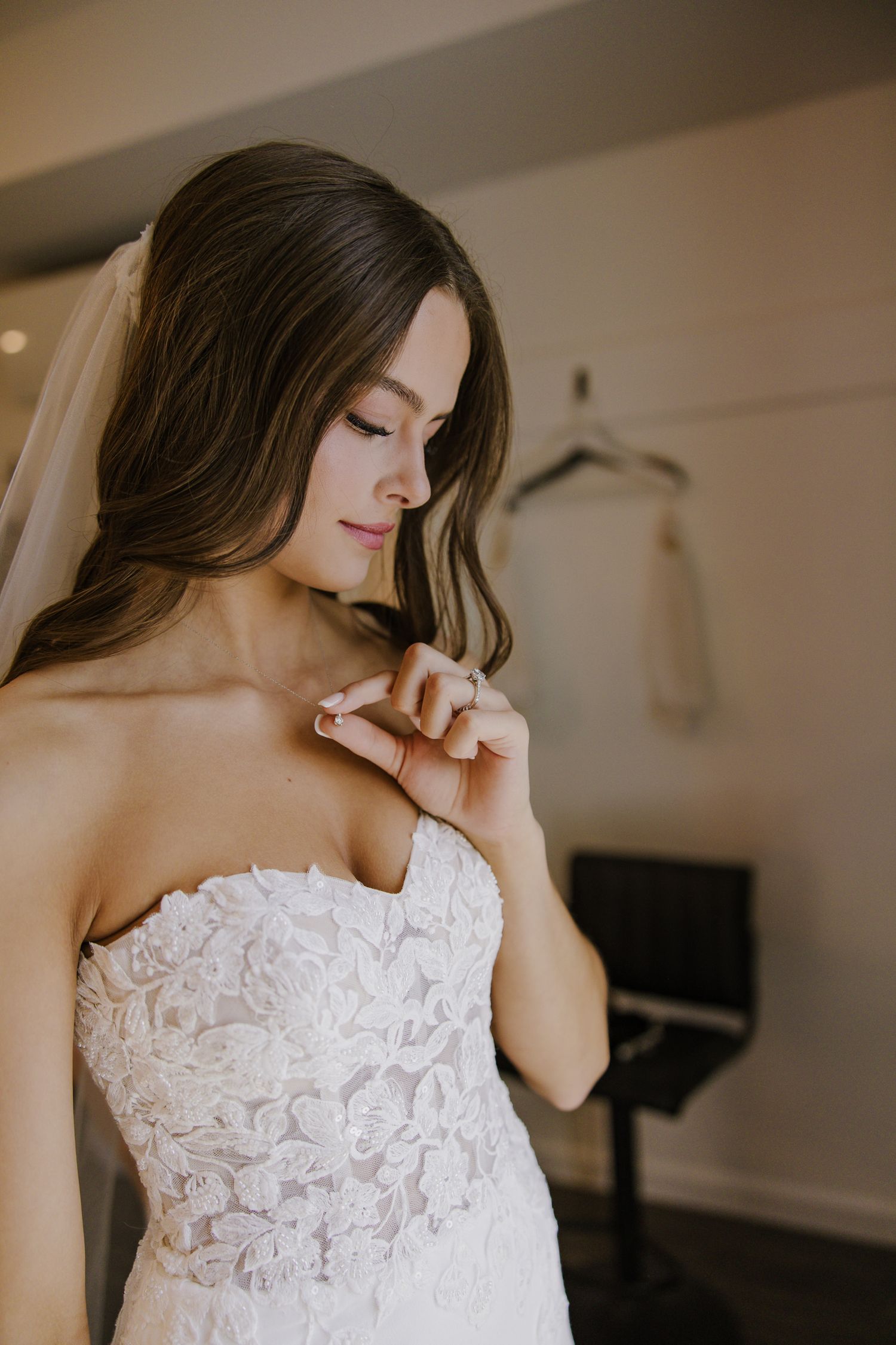 A bride wearing a detailed lace wedding gown poses in a getting ready room.