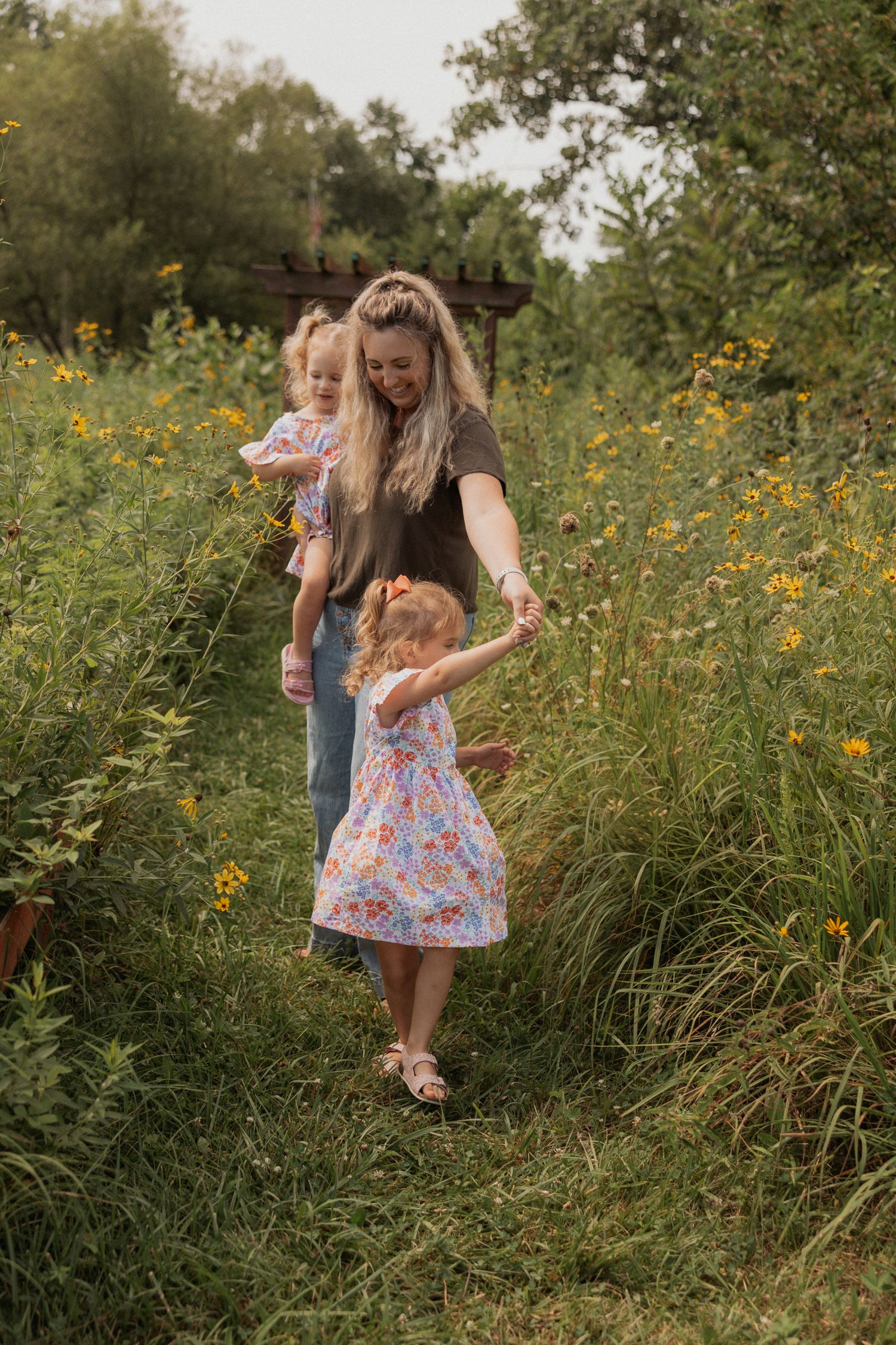 Family walking along a grassy path surrounded by yellow wildflowers and trees.
