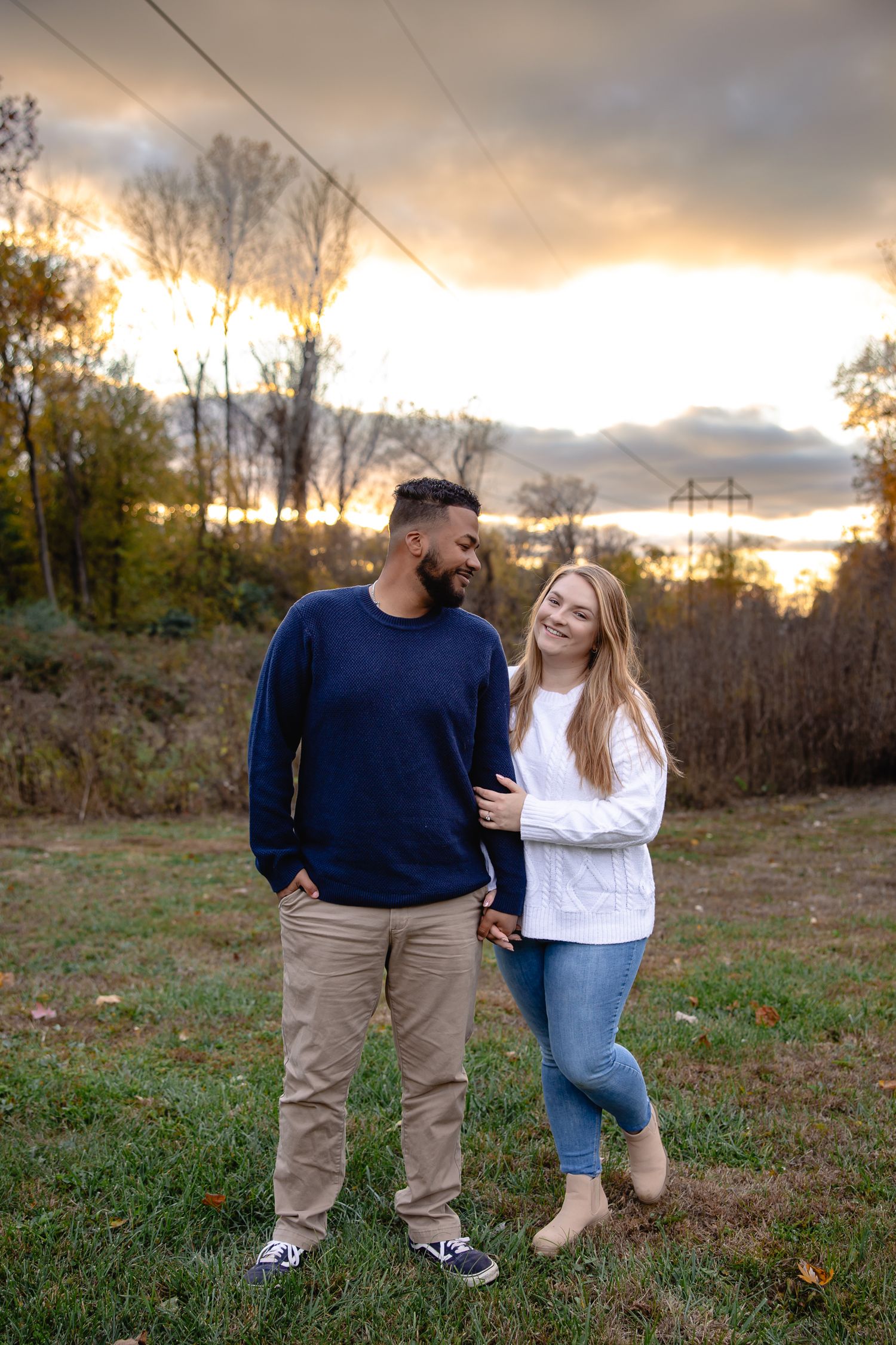 Sunset engagement session in a rustic field showing couple in casual attire.