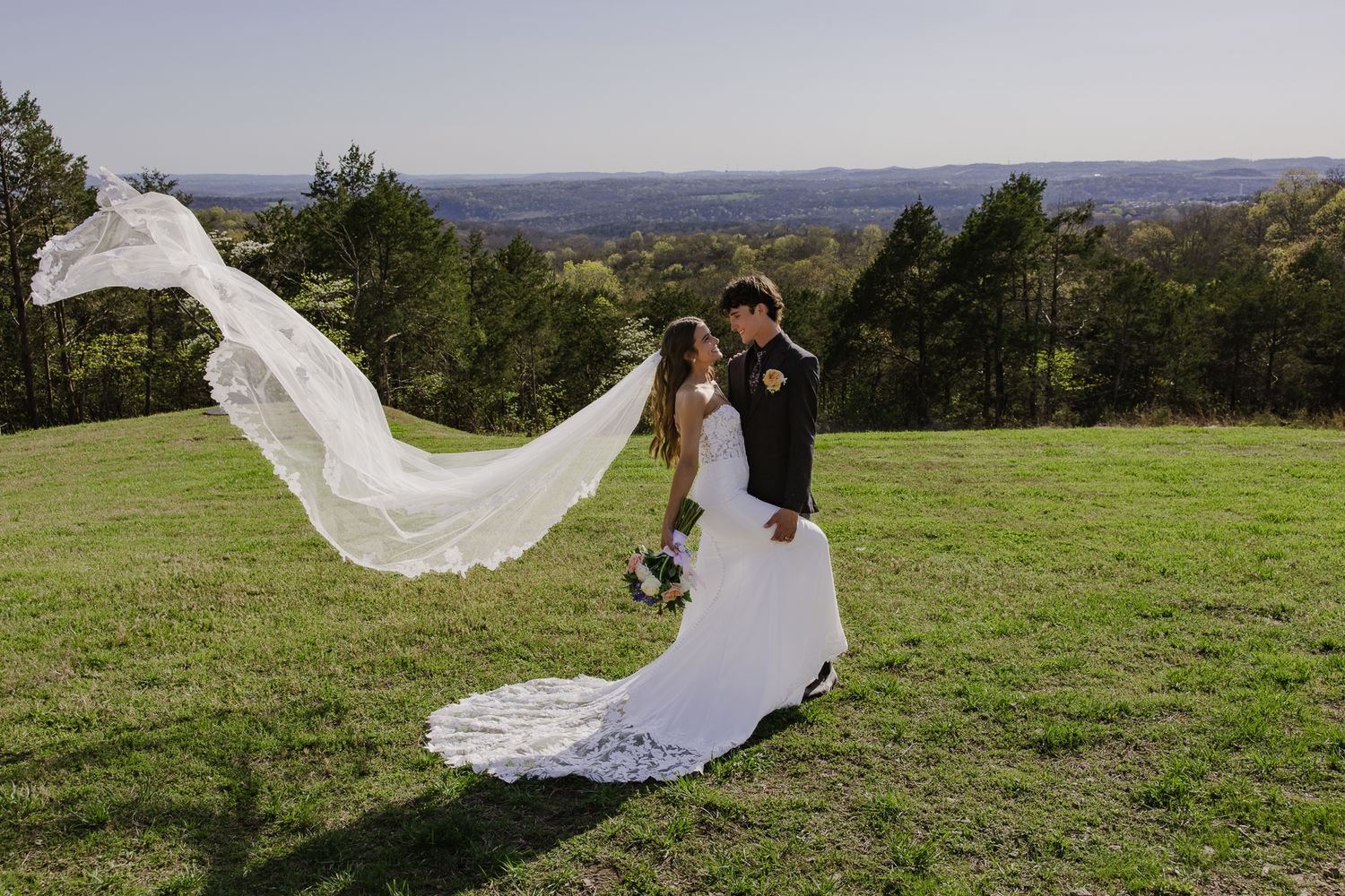 A dramatic wedding photo showing a flowing veil catching wind on a scenic hilltop.