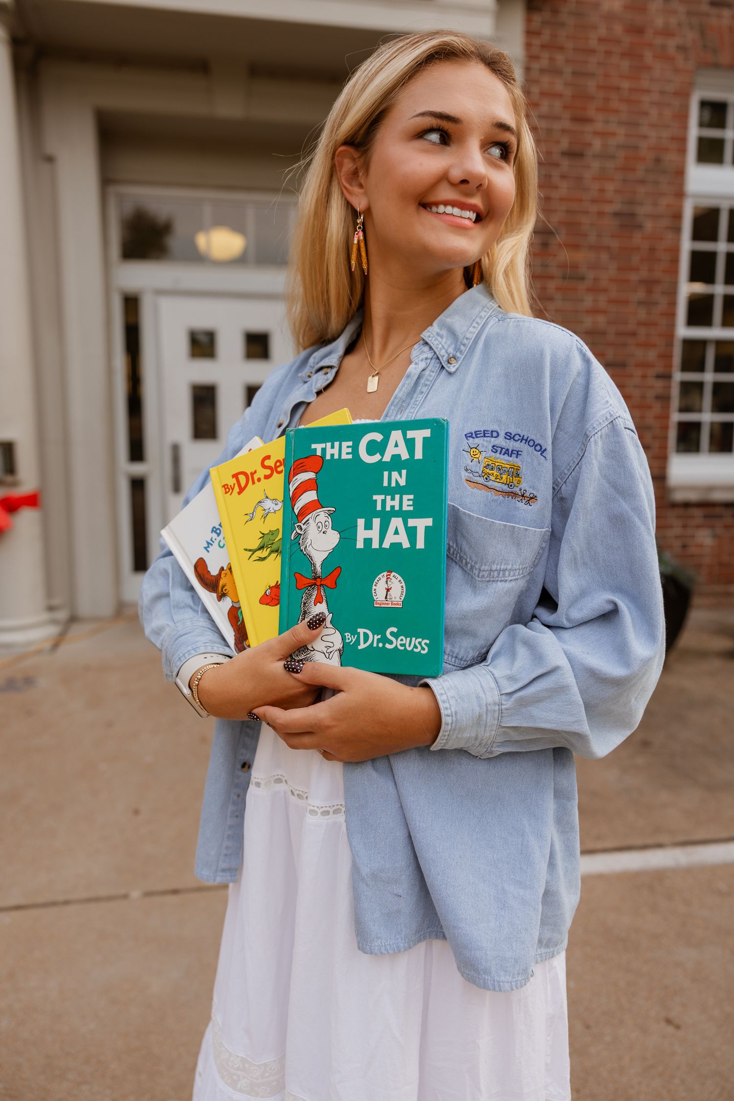 Someone holds beloved Dr. Seuss books while standing in front of a traditional school building.