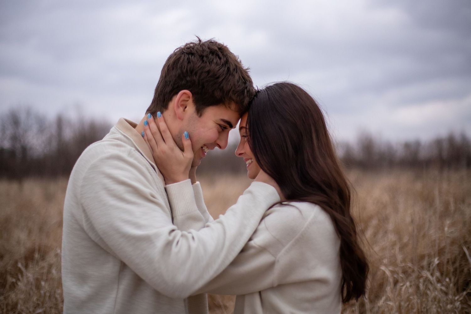 Romantic couple embraces tenderly in a field of tall grass under moody overcast skies.