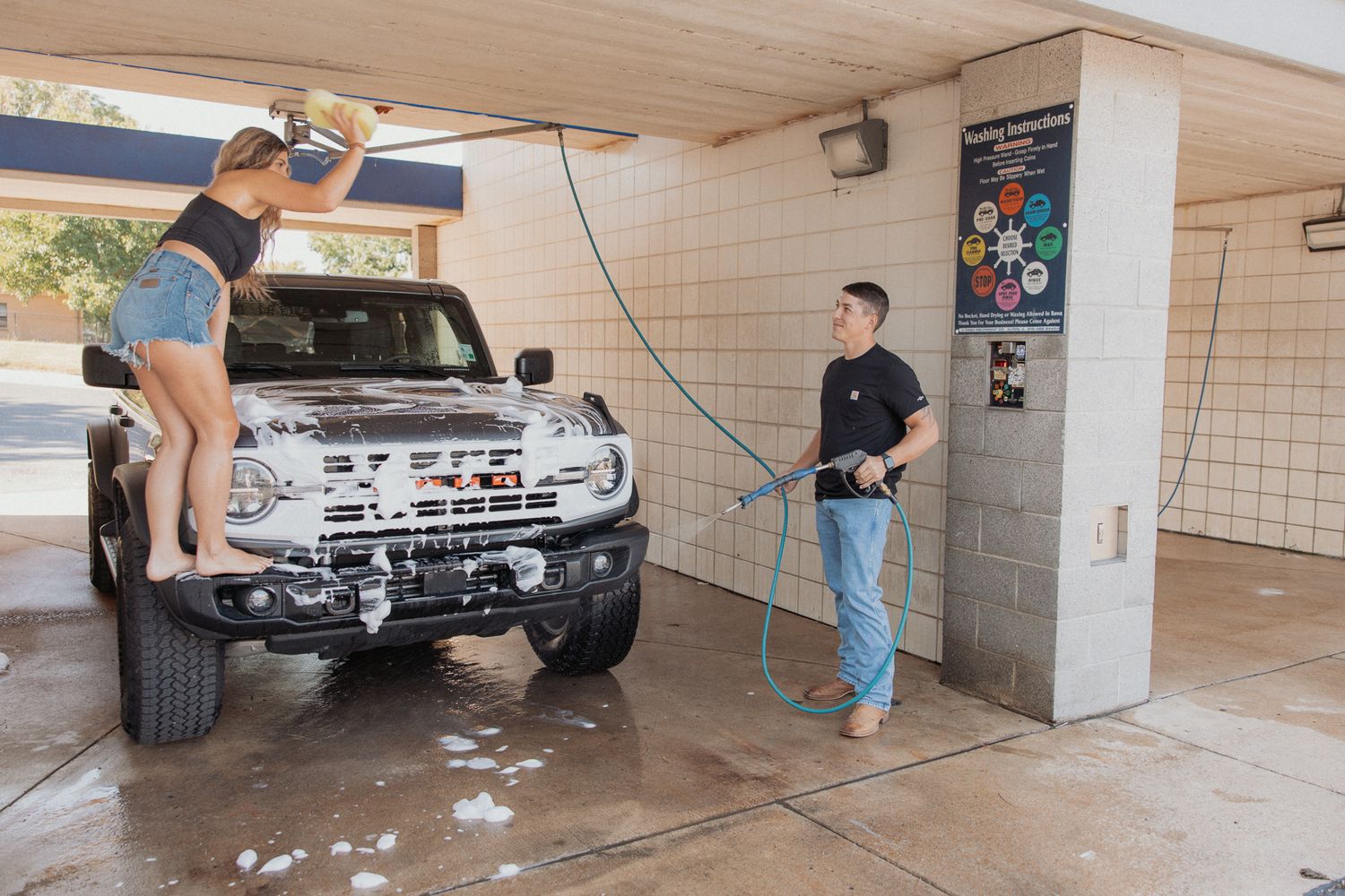 People gathered around a parked Ford Bronco in covered parking garage setting.