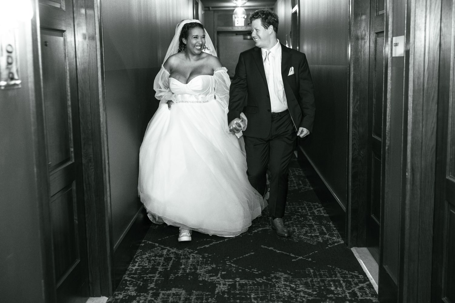 Wedding party walks down a dimly lit hotel hallway in formal attire.