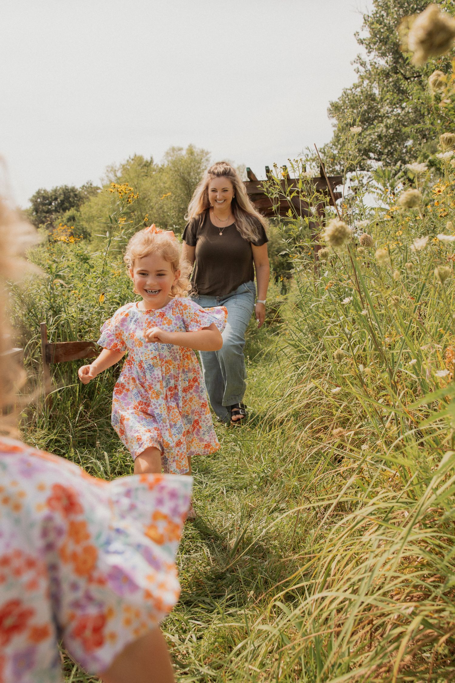 A child in a floral dress runs through tall grass on a sunny day.