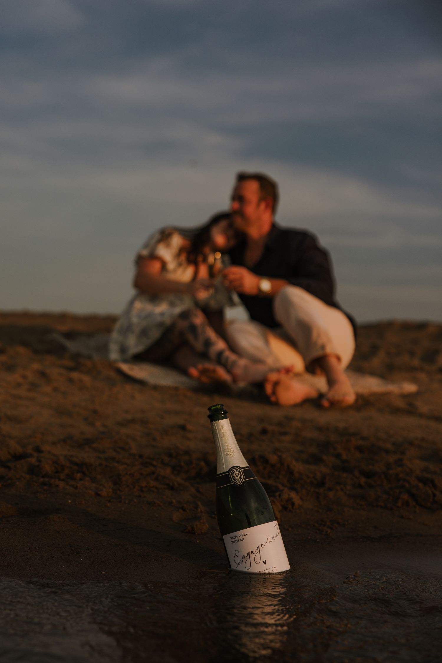 Champagne bottles on beach sand during romantic sunset photoshoot.