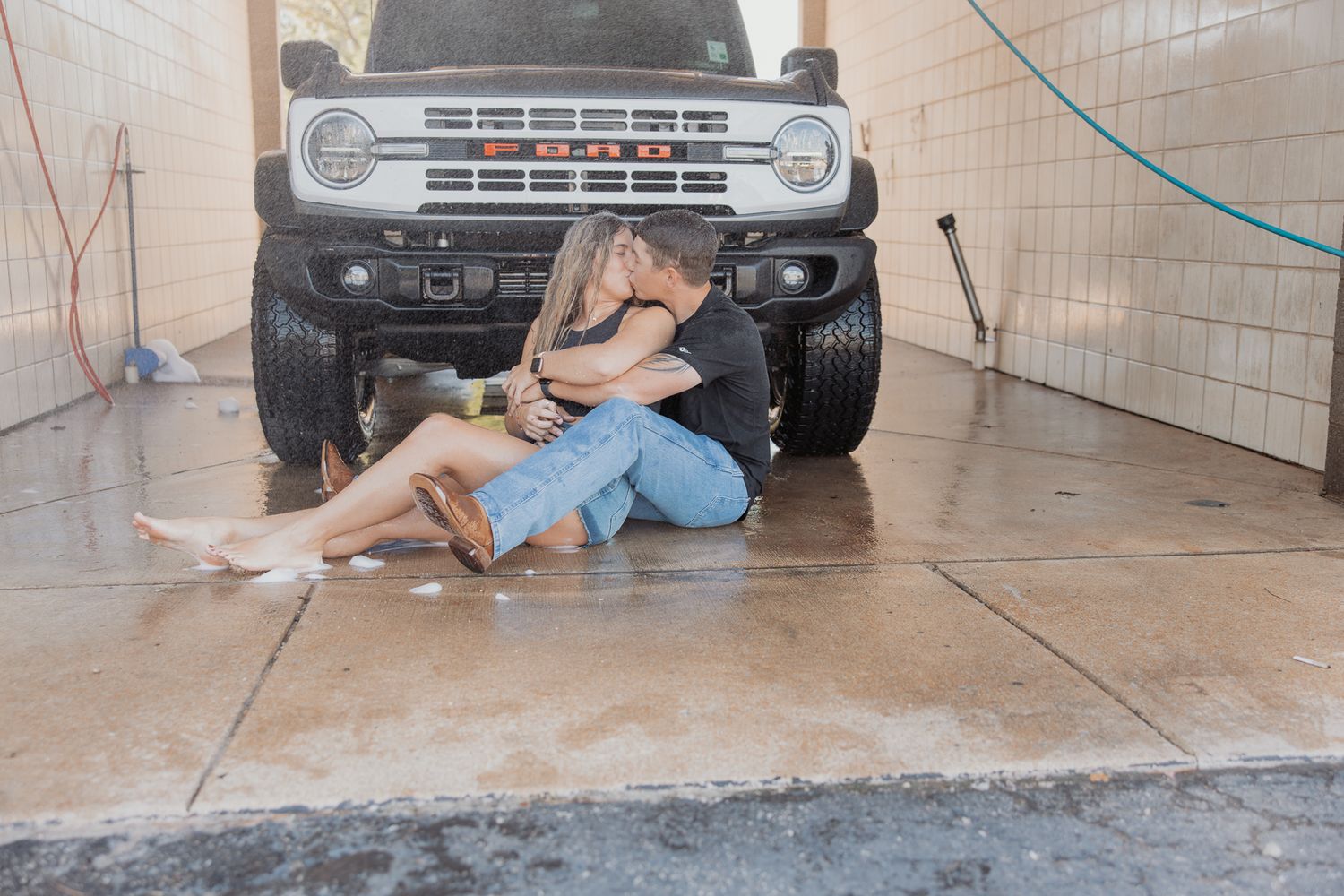 Intimate moment shared in front of classic white Ford Bronco in garage setting.