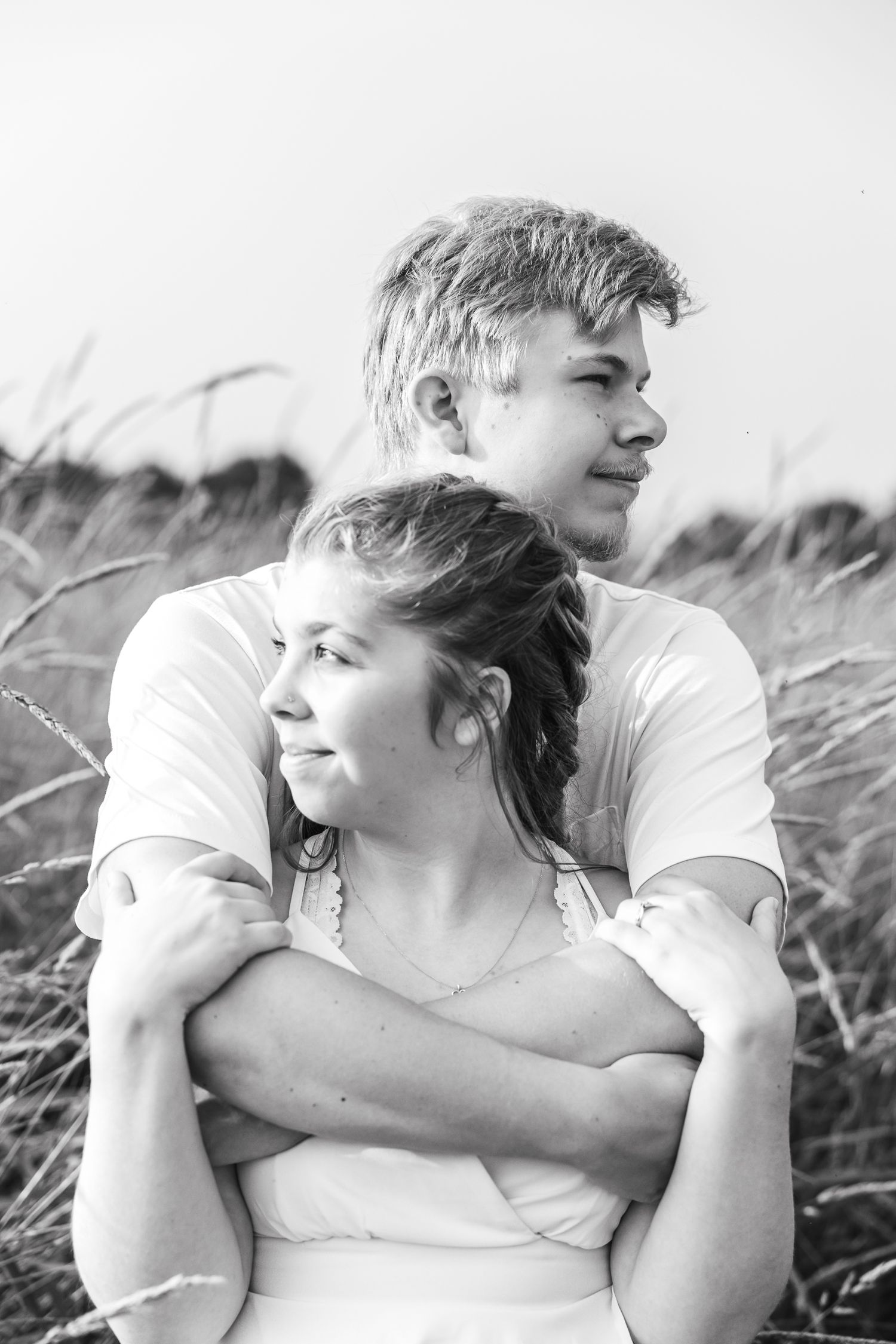 High contrast black and white photos of couple embracing in field of tall grass.