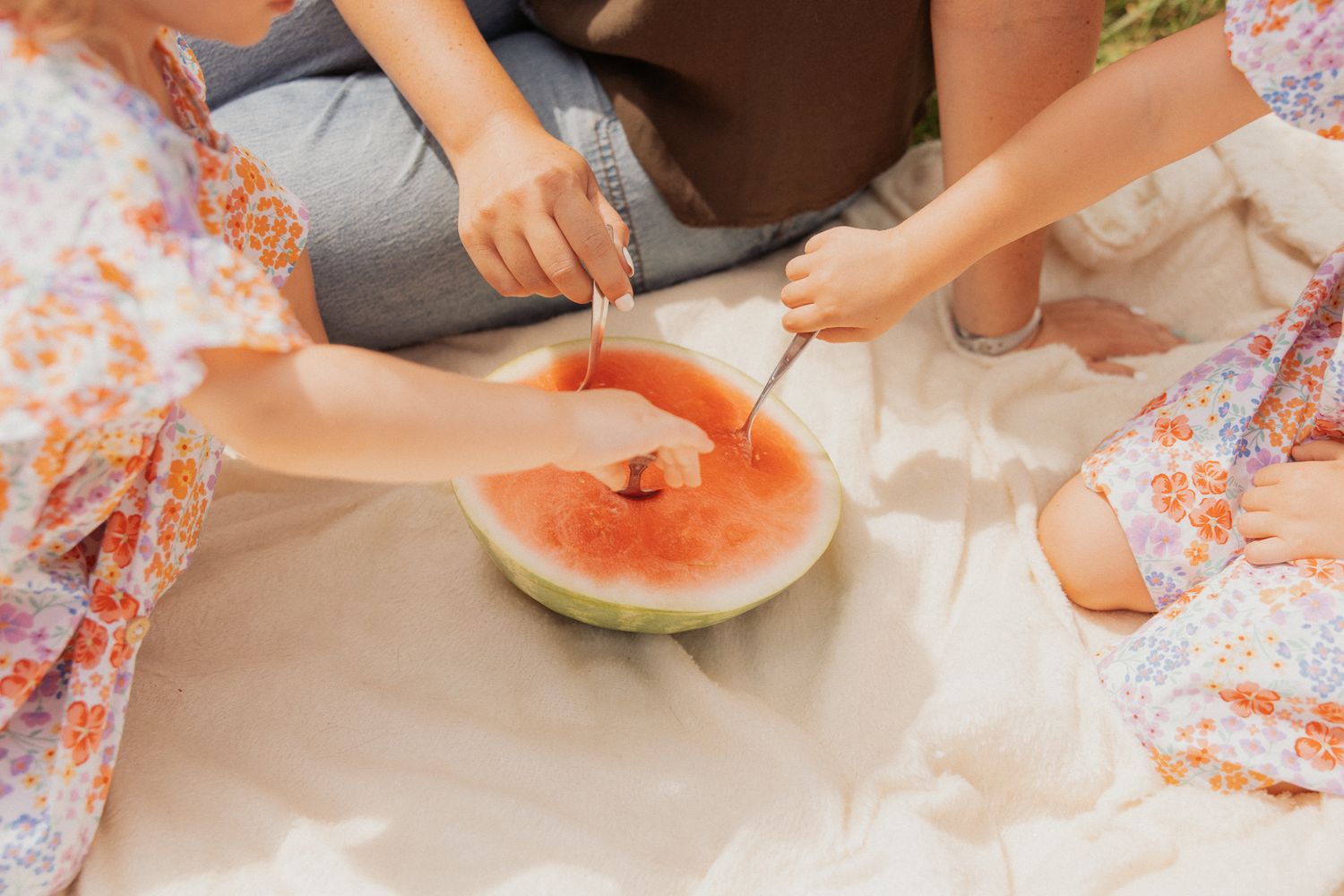 Hands cutting into a fresh watermelon during an outdoor summer picnic.