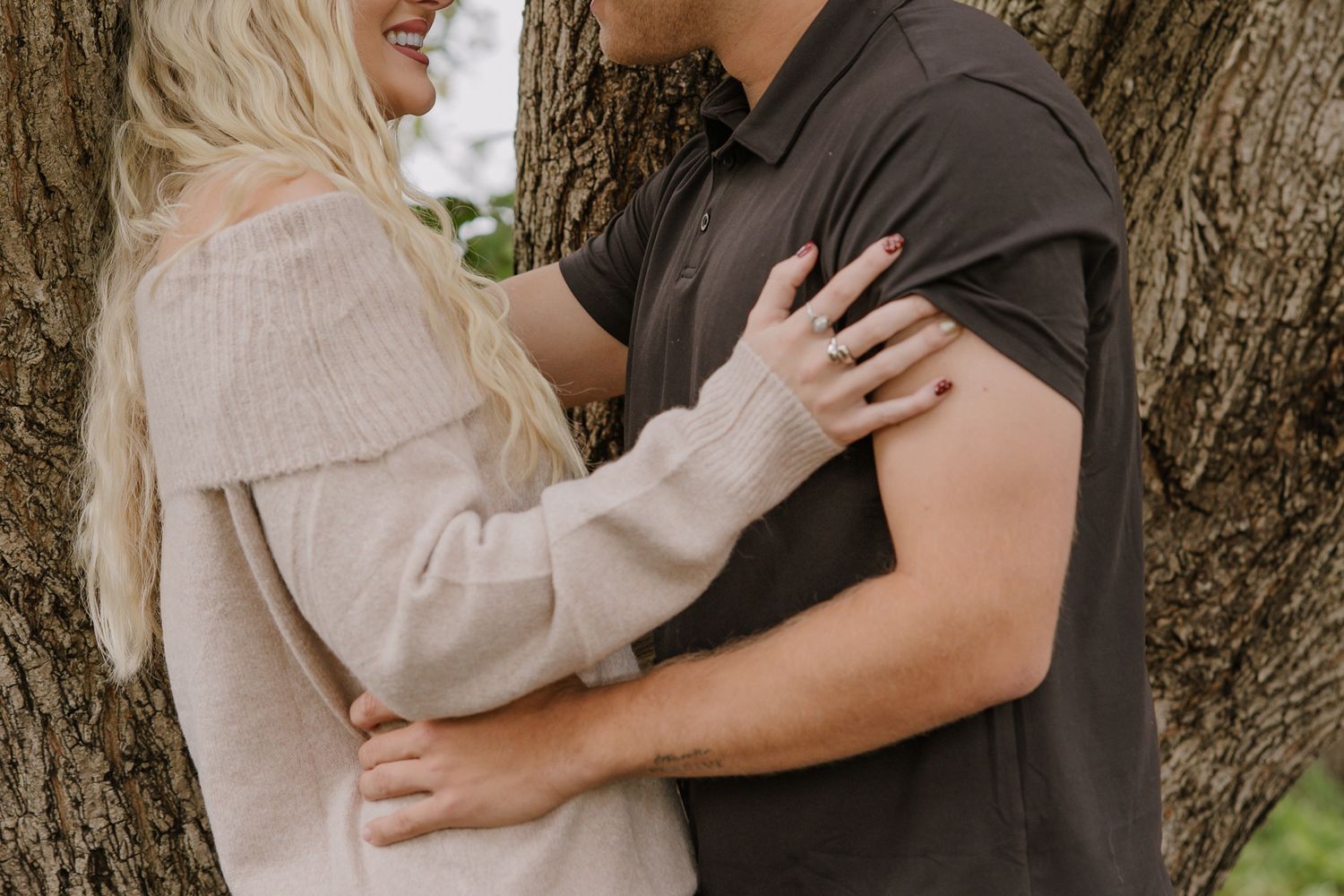 Couple embracing and laughing together while standing against a tree trunk.