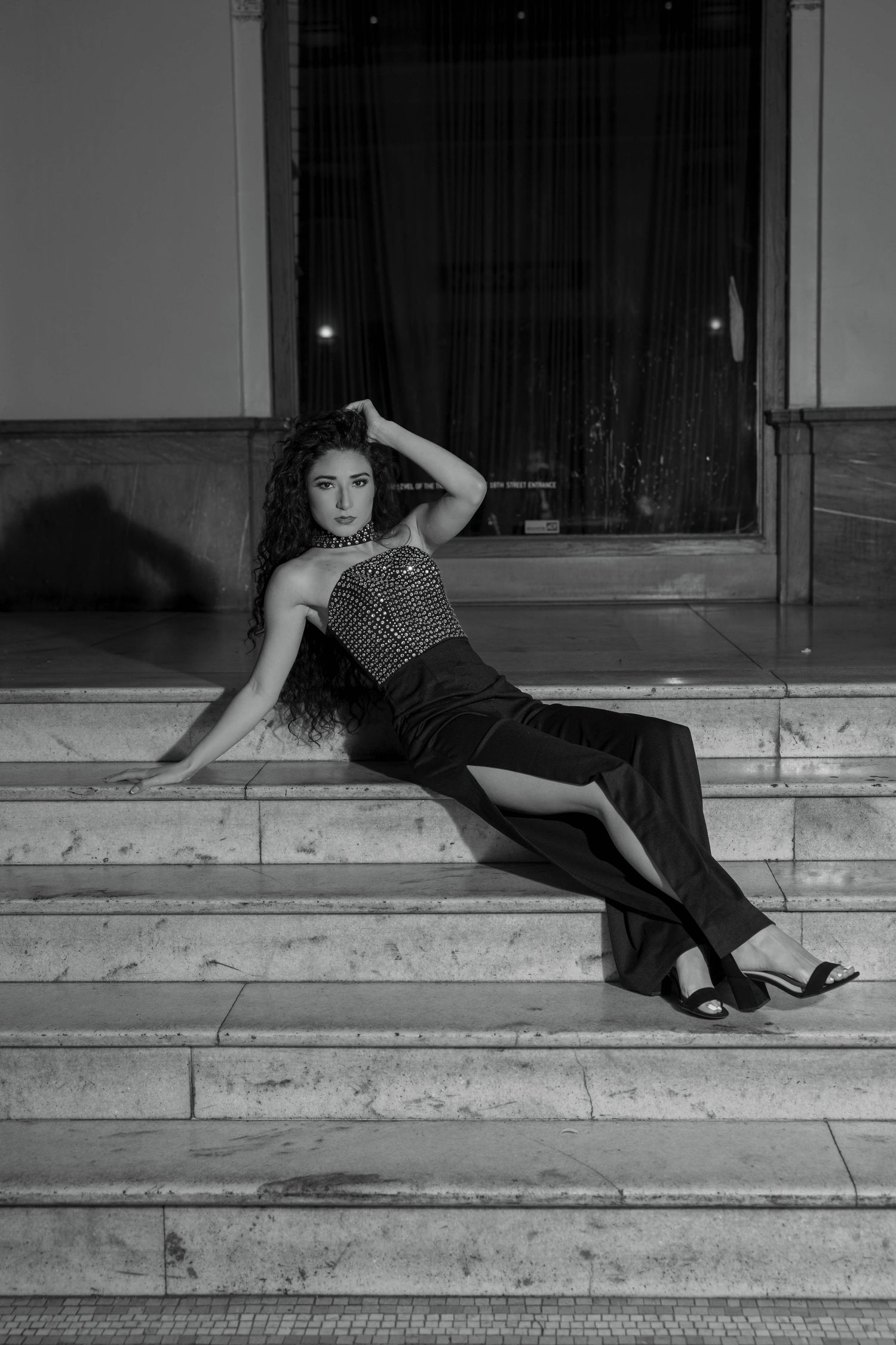 Woman in sequined top and black pants posing on marble steps in black and white photo.