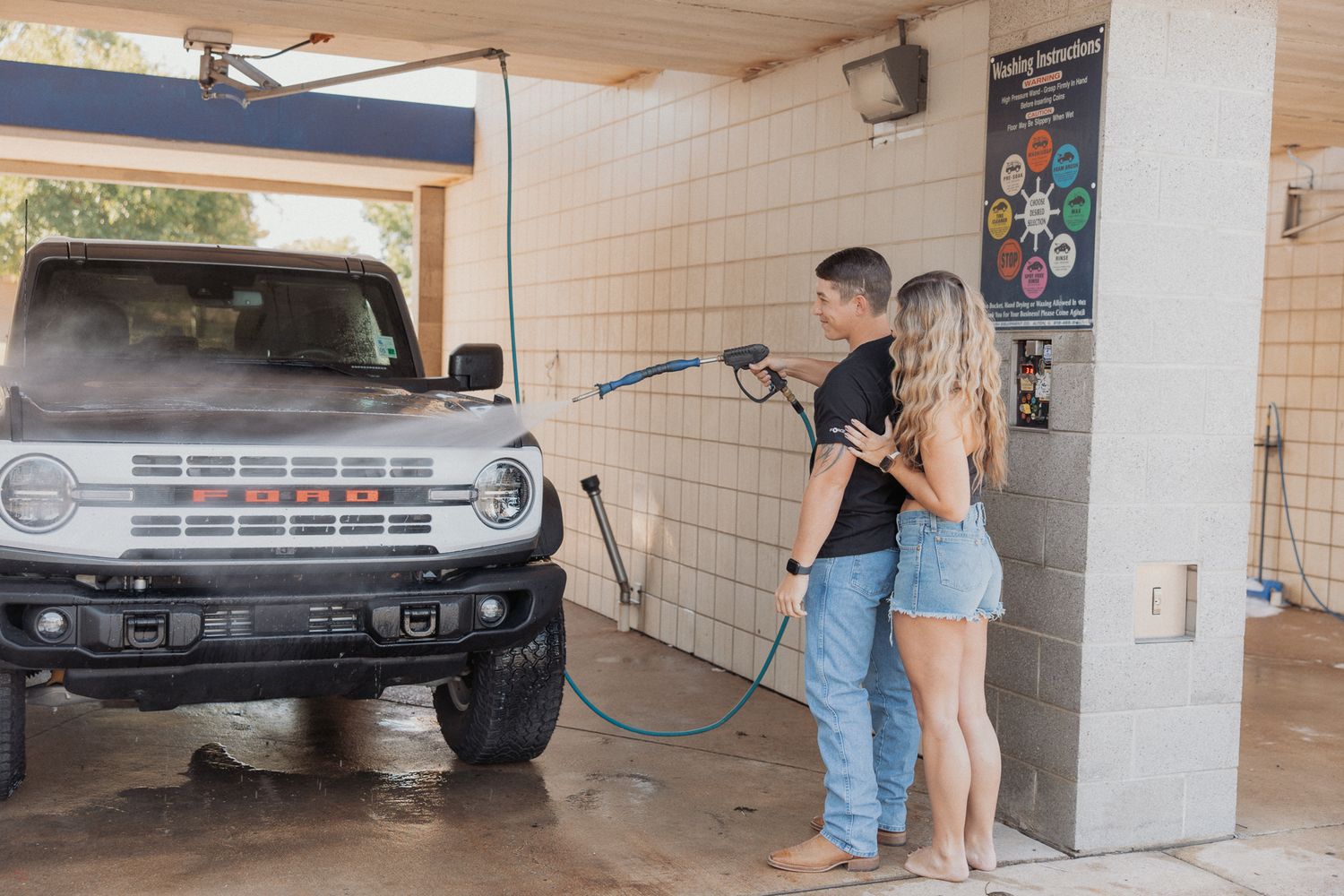 A couple at a car wash facility with a truck being cleaned in the background.