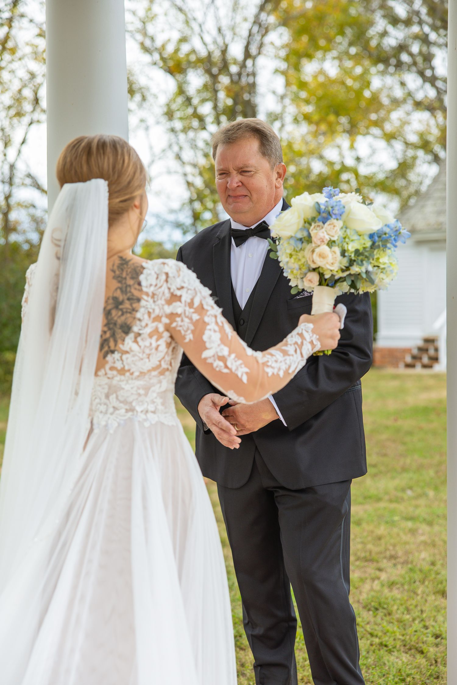 Intimate wedding moment captured under white columns with spring flowers.