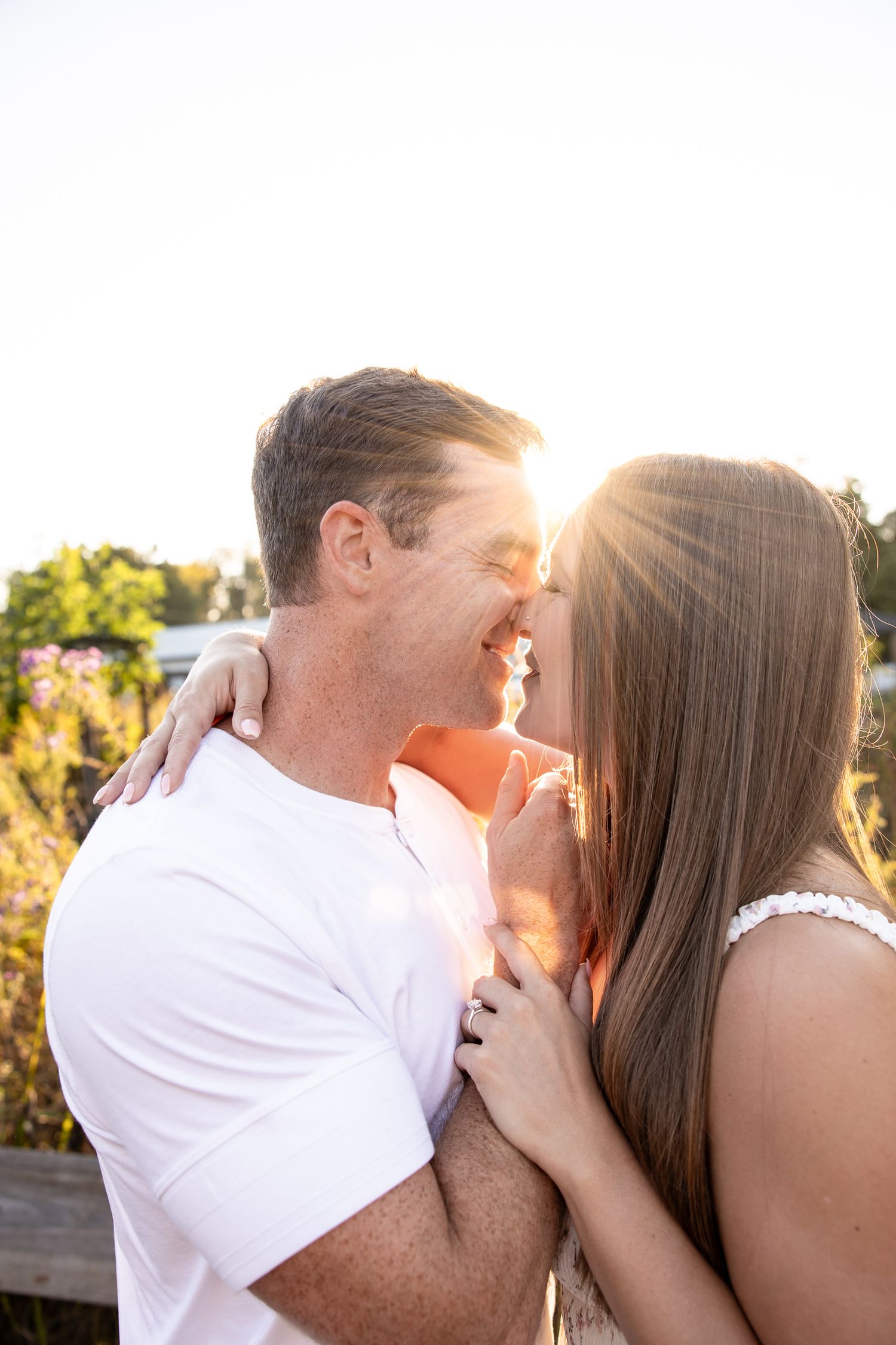 Couple shares intimate kisses against golden sunlight in outdoor setting.
