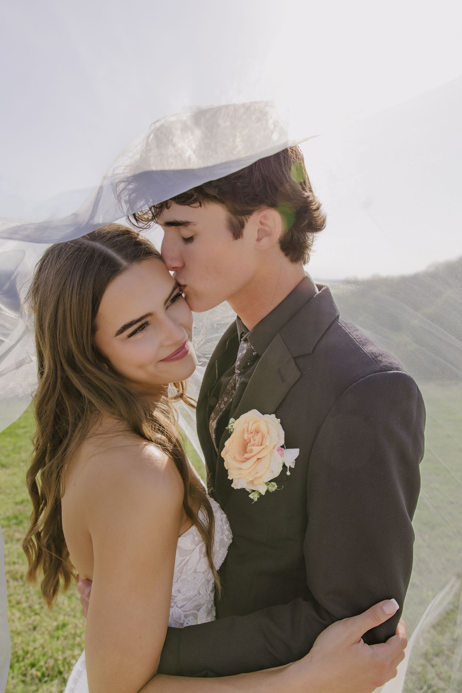 Sun-kissed wedding portraits against mountain backdrop with bride in lace dress and groom in dark suit.