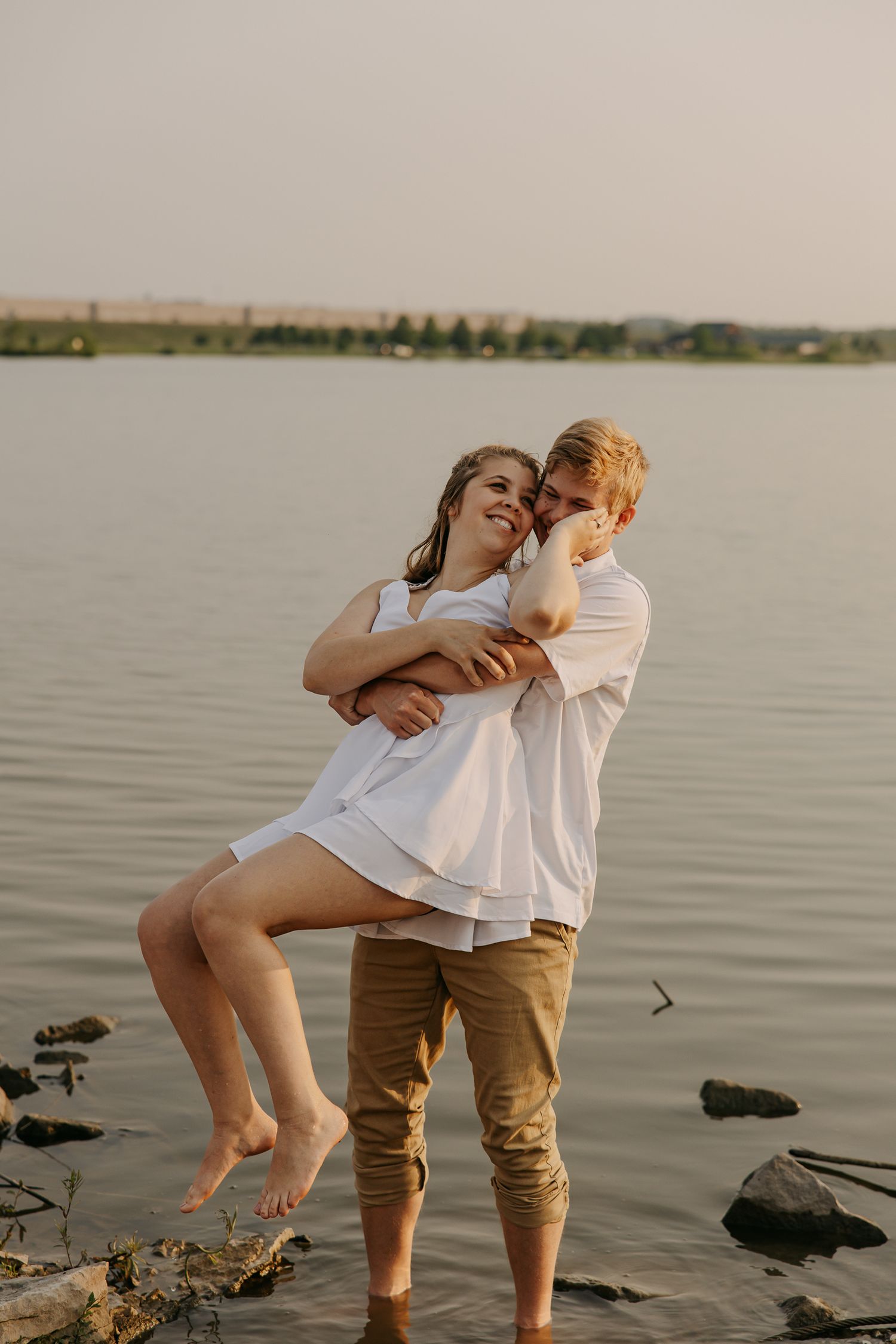 Playful couple interacts on shoreline during sunset photoshoot.