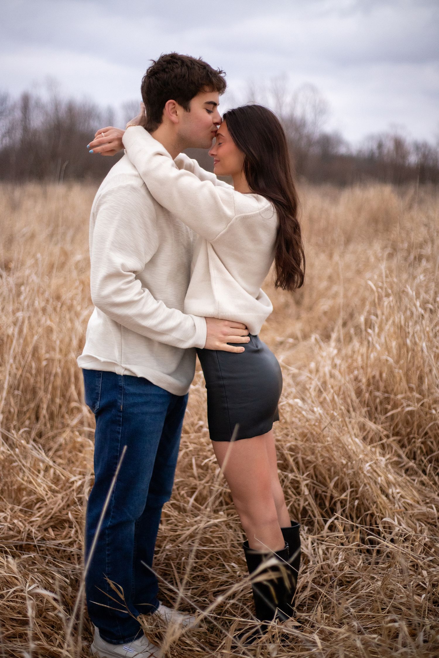 Couple shares an intimate moment in a field of tall brown grass on an overcast day.