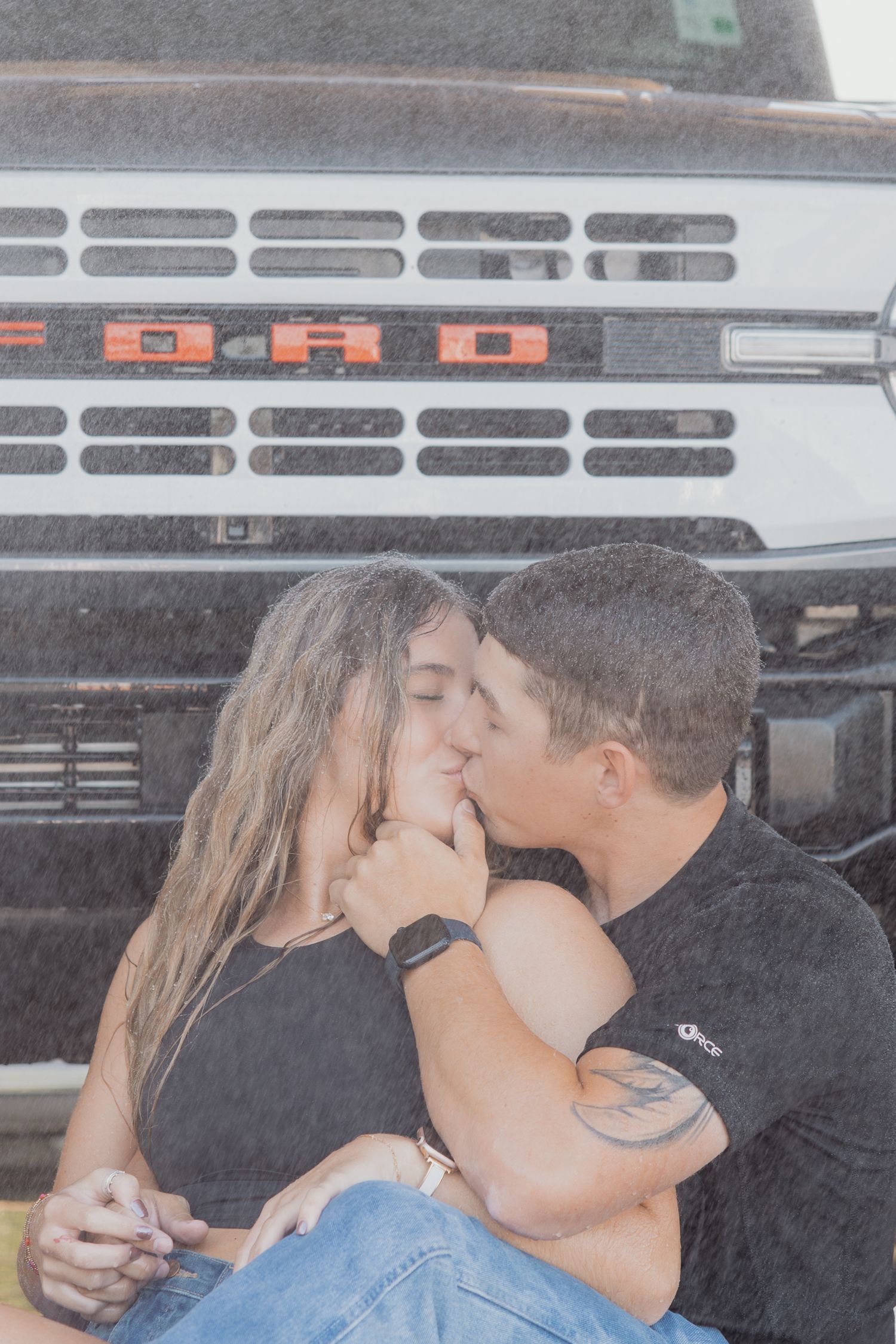 Romantic moment shared in front of Ford truck grille on rainy day.