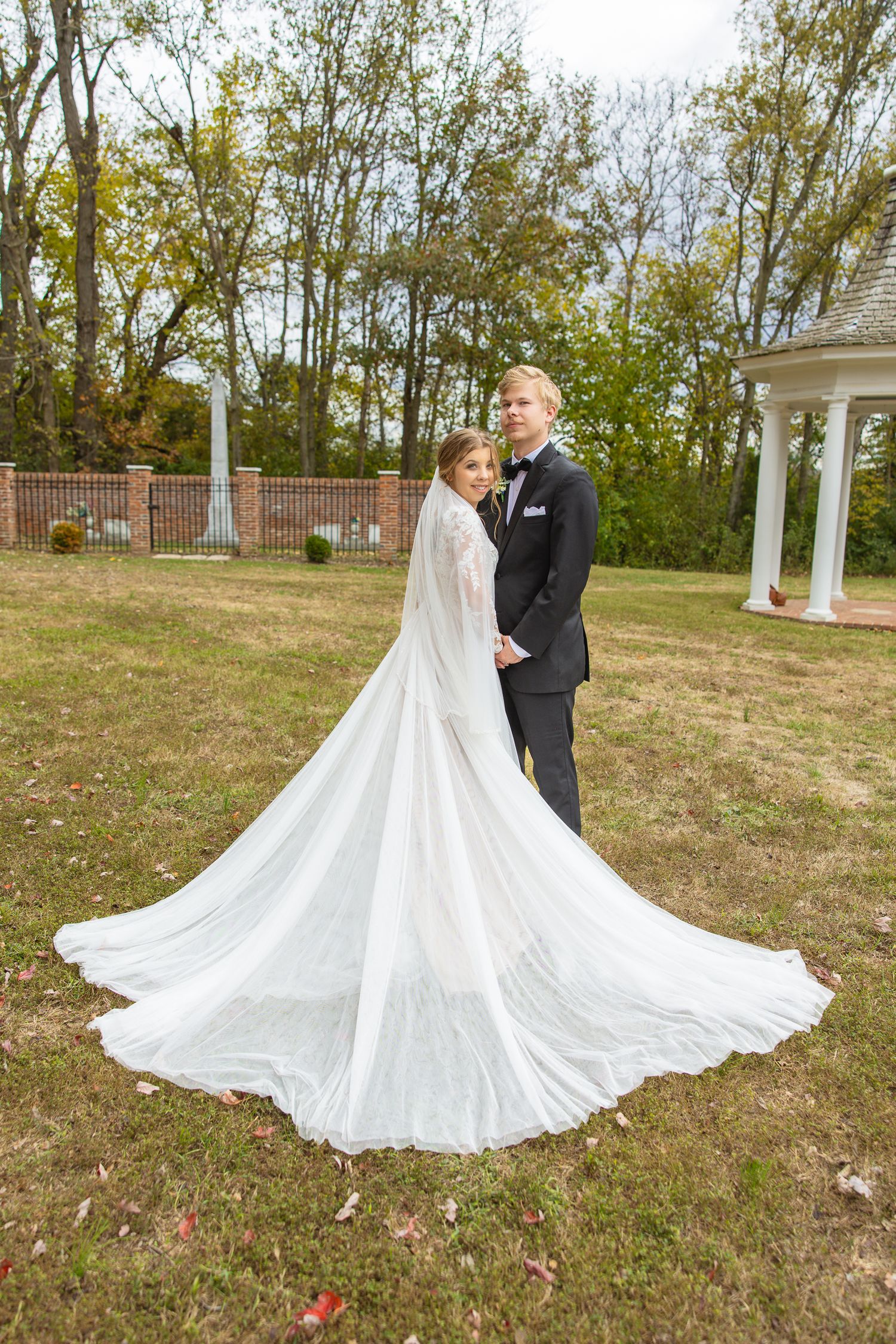Bride's dramatic cathedral veil flows in the wind during outdoor autumn wedding portraits.