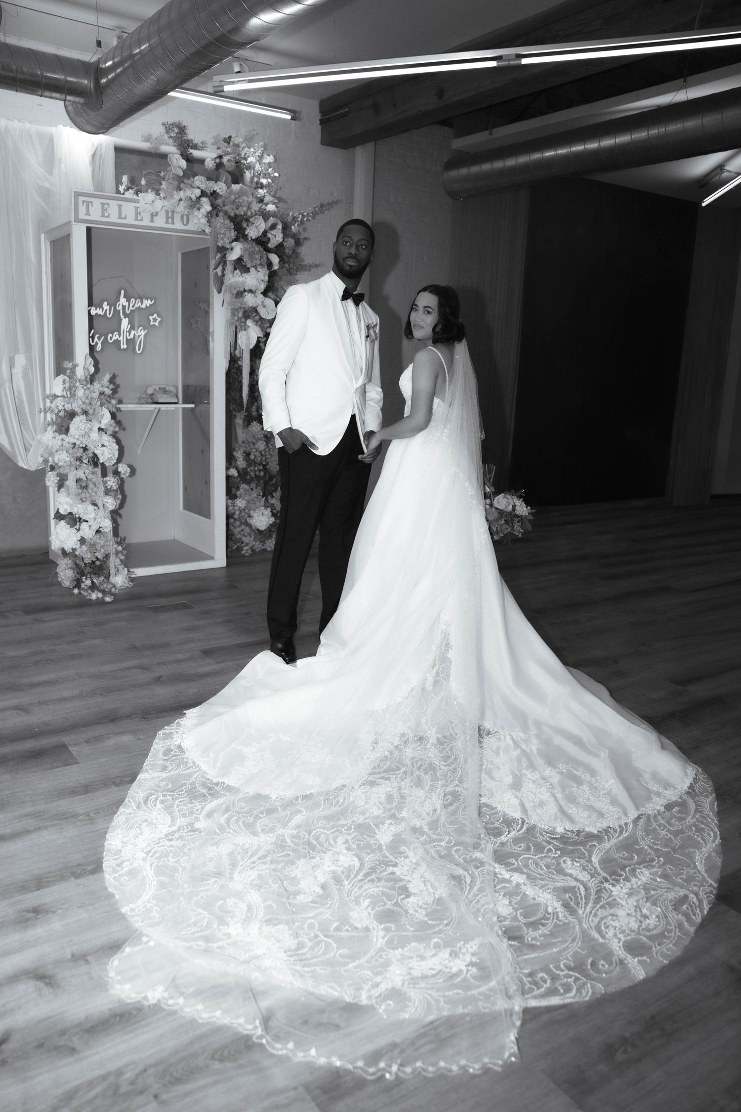 Wedding couple posing by floral arch showing off bride's long lace train.