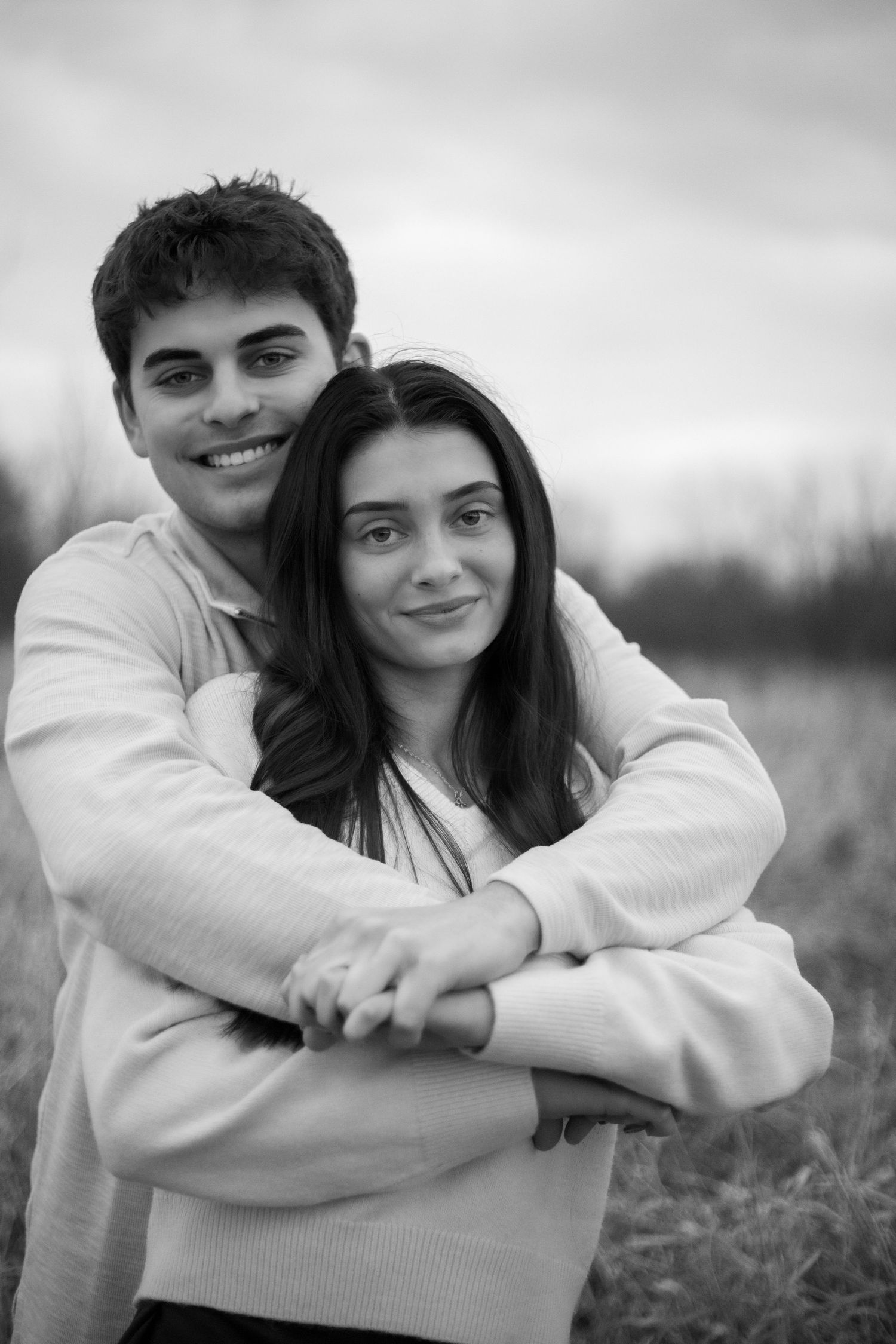 Black and white portraits of couple embracing in casual sweaters outdoors.