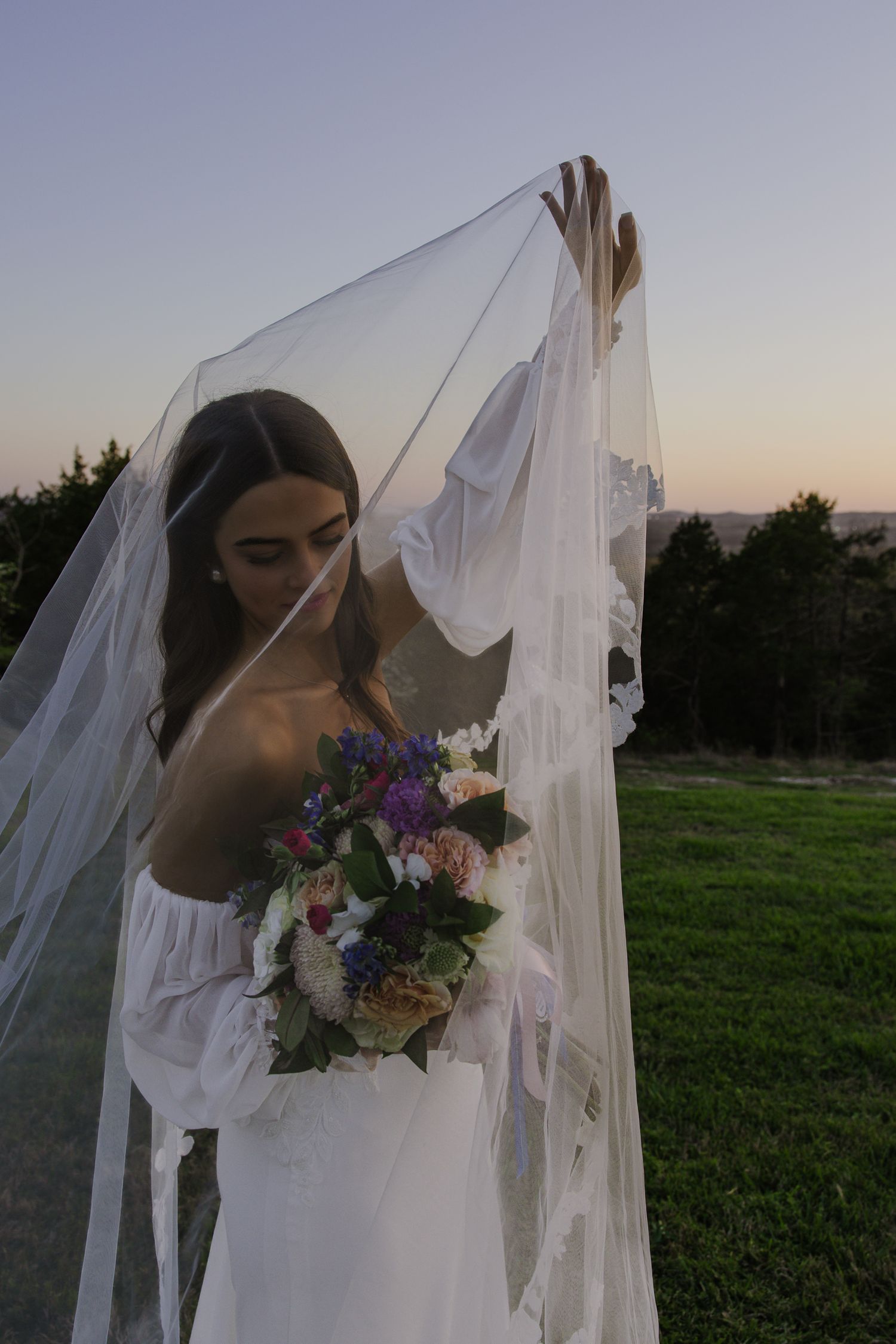 Ethereal bridal portraits in a field at sunset with flowing white veil and vibrant wedding bouquet.