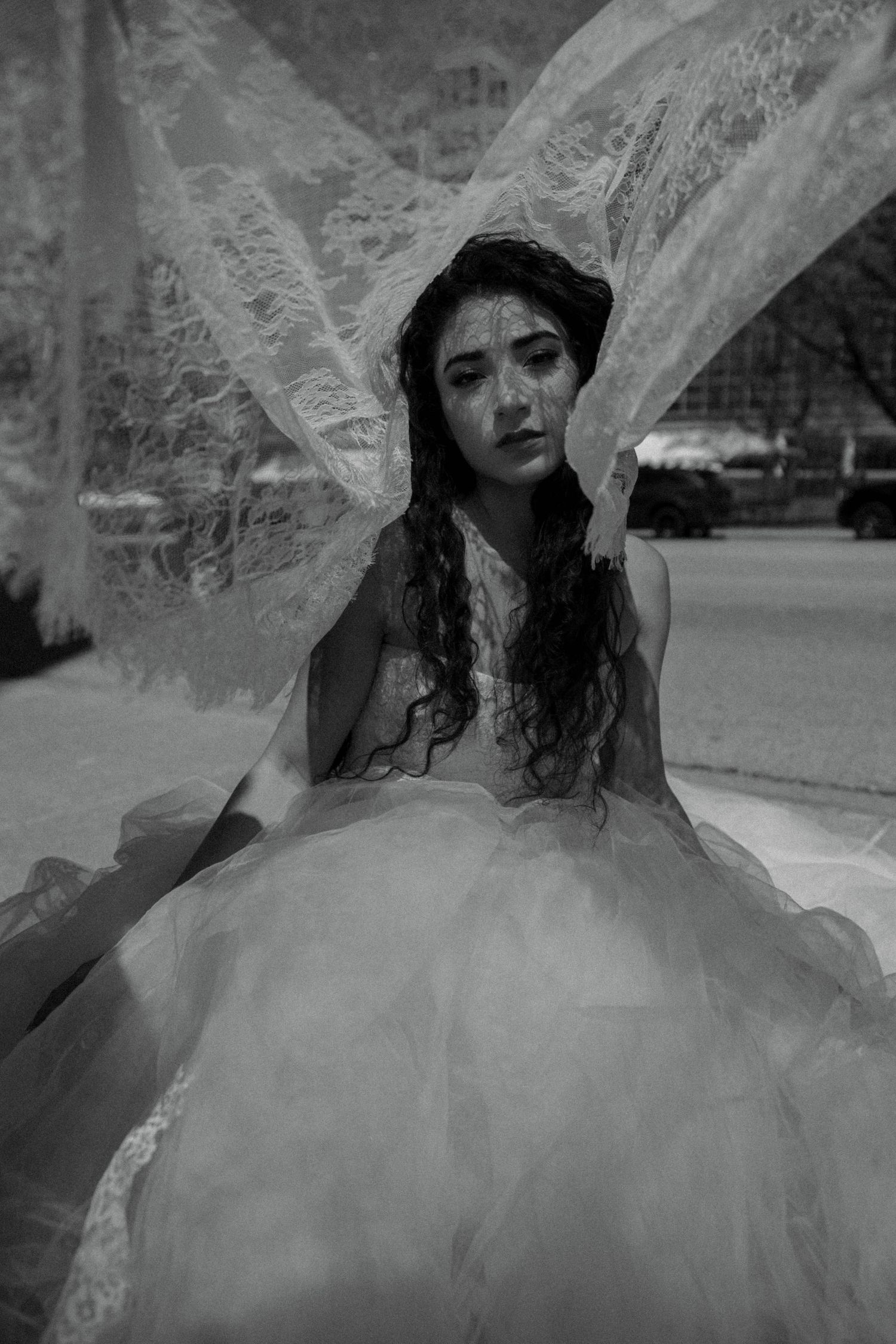 Black and white portrait of a bride in tulle ball gown with lace veil billowing dramatically around her.