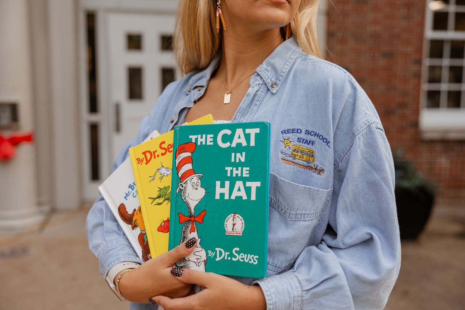 Someone holds Dr. Seuss books including The Cat in the Hat while wearing a denim jacket.