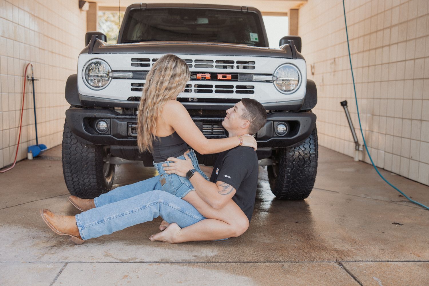 Couple posing playfully on garage floor in front of classic truck.