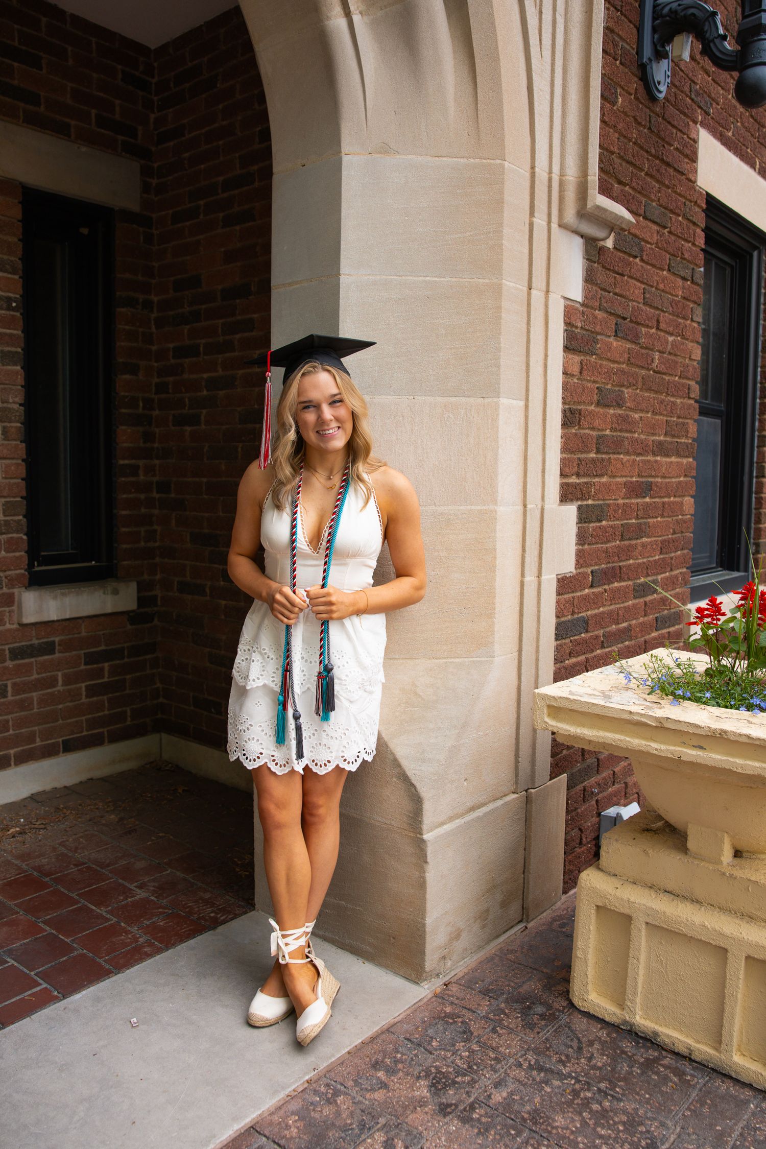 Person in white dress poses near ornate stone columns of traditional brick building entrance.