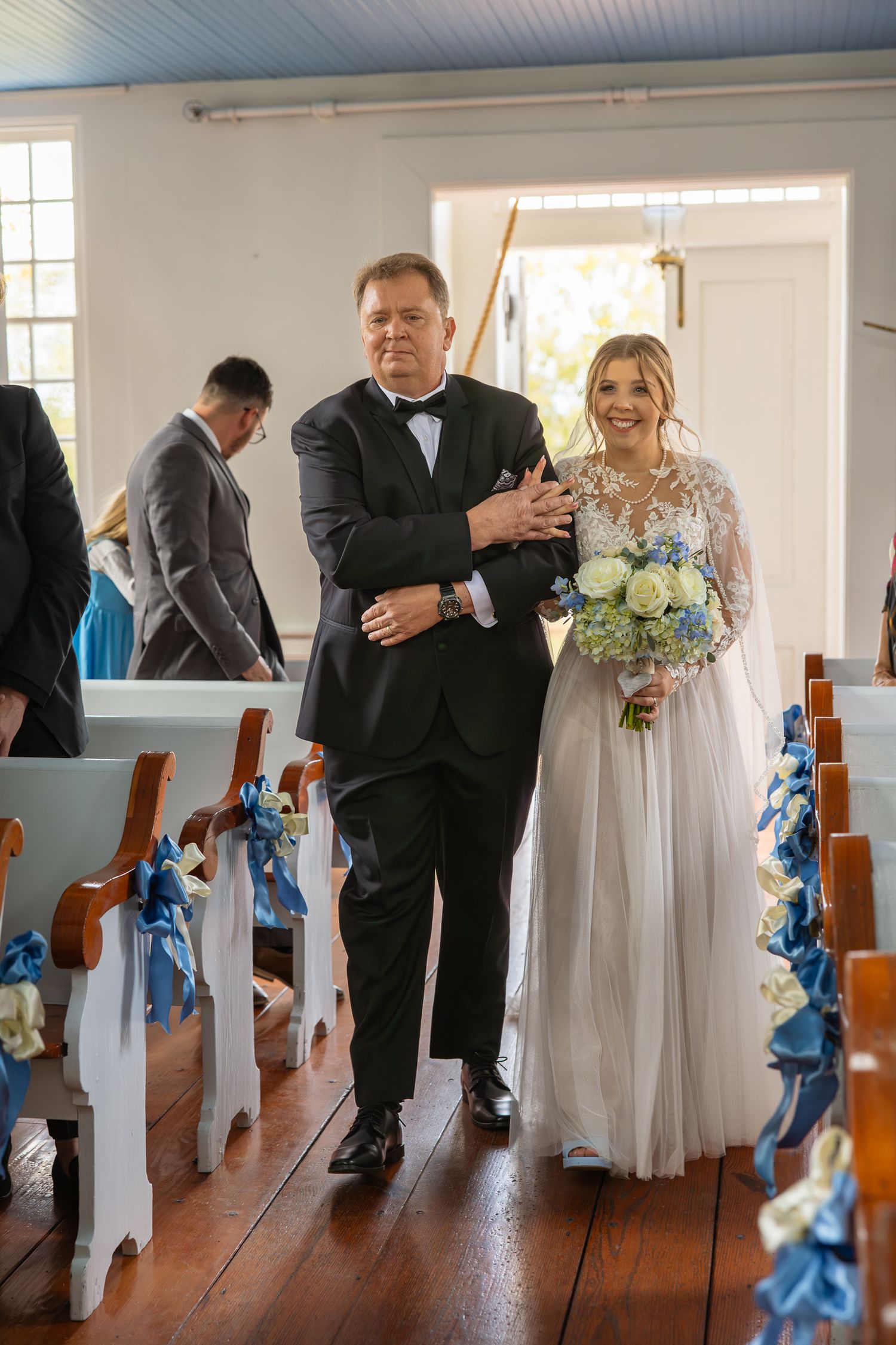 Wedding ceremony procession in a bright white chapel with blue decorative ribbons.