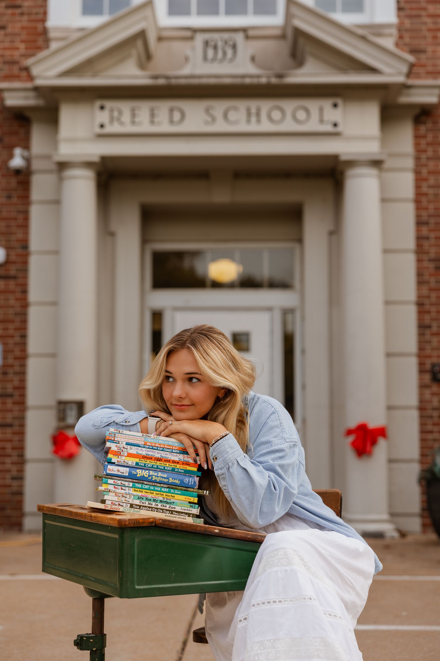 A peaceful reading scene with stacked books outside a traditional brick schoolhouse entrance.