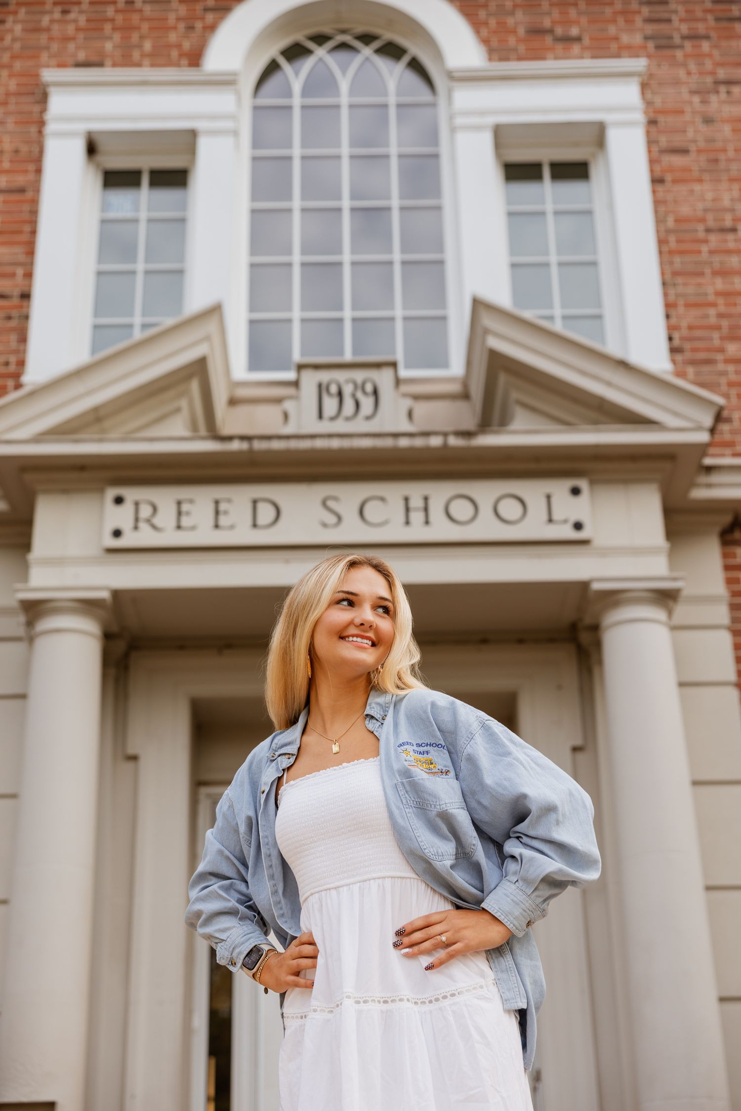 A person in a denim jacket stands in front of Reed School's brick facade and white columns.